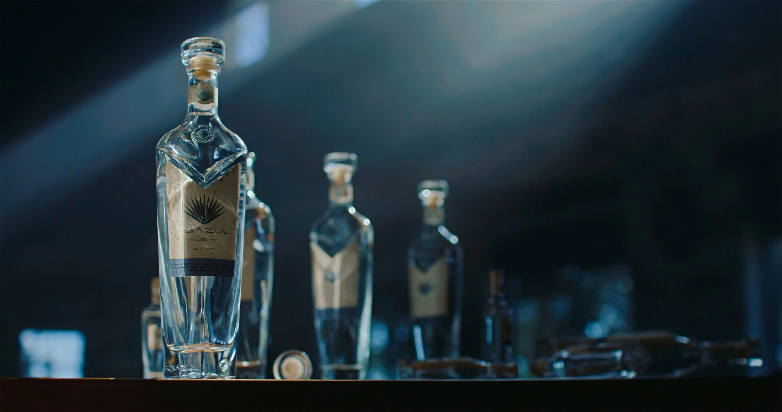 Agazul tequila bottles displayed on a bar in a haze filled room on joey arcisz portfolio website
