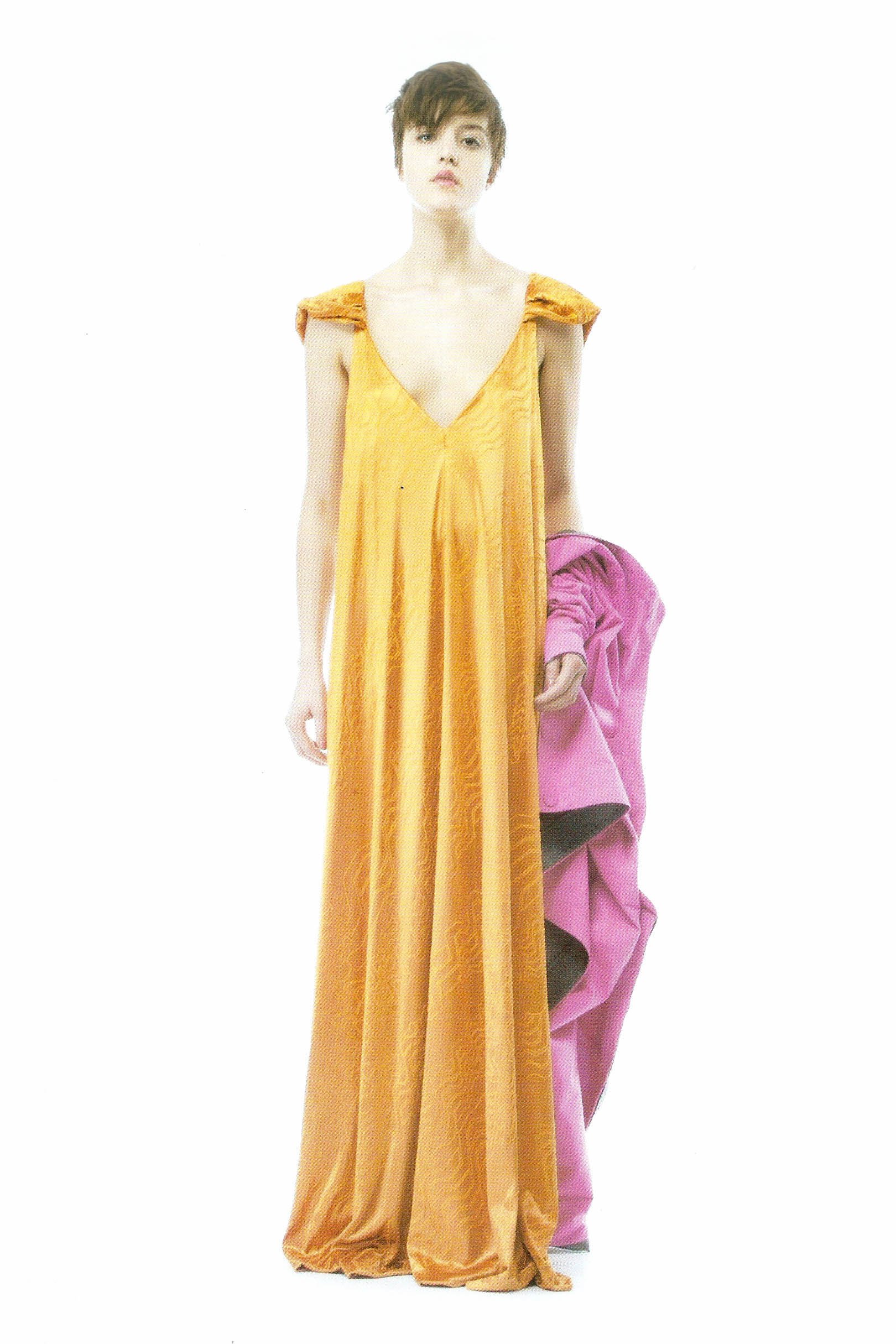 A mannequin wearing a long, flowing yellow dress with shoulder details, standing against a white background, holding a purple garment.