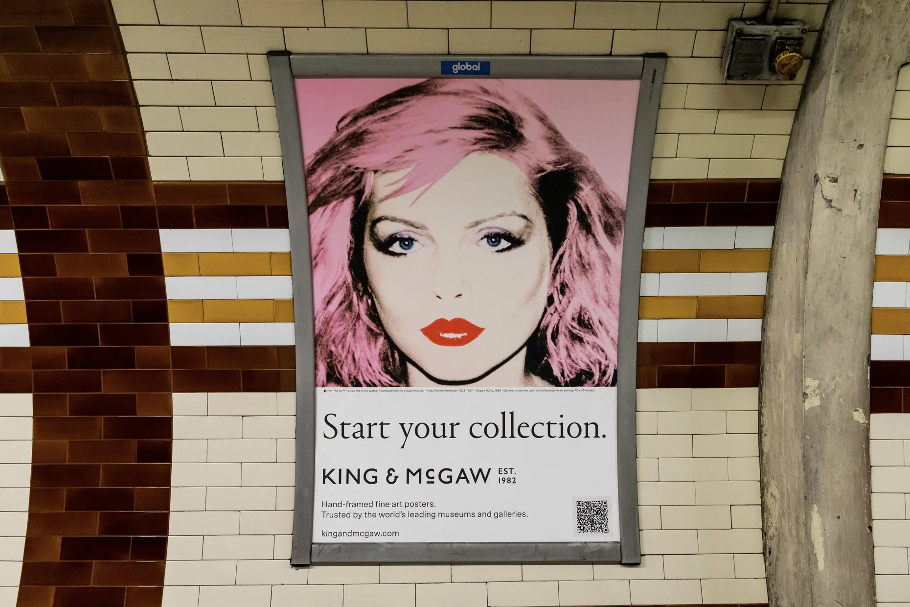A poster featuring a stylized portrait of a woman with short pink hair, blue eyes, and red lipstick. The poster promotes starting a collection through King & McGaw, with text beneath the image that reads, 'Start your collection,' and mentions the com