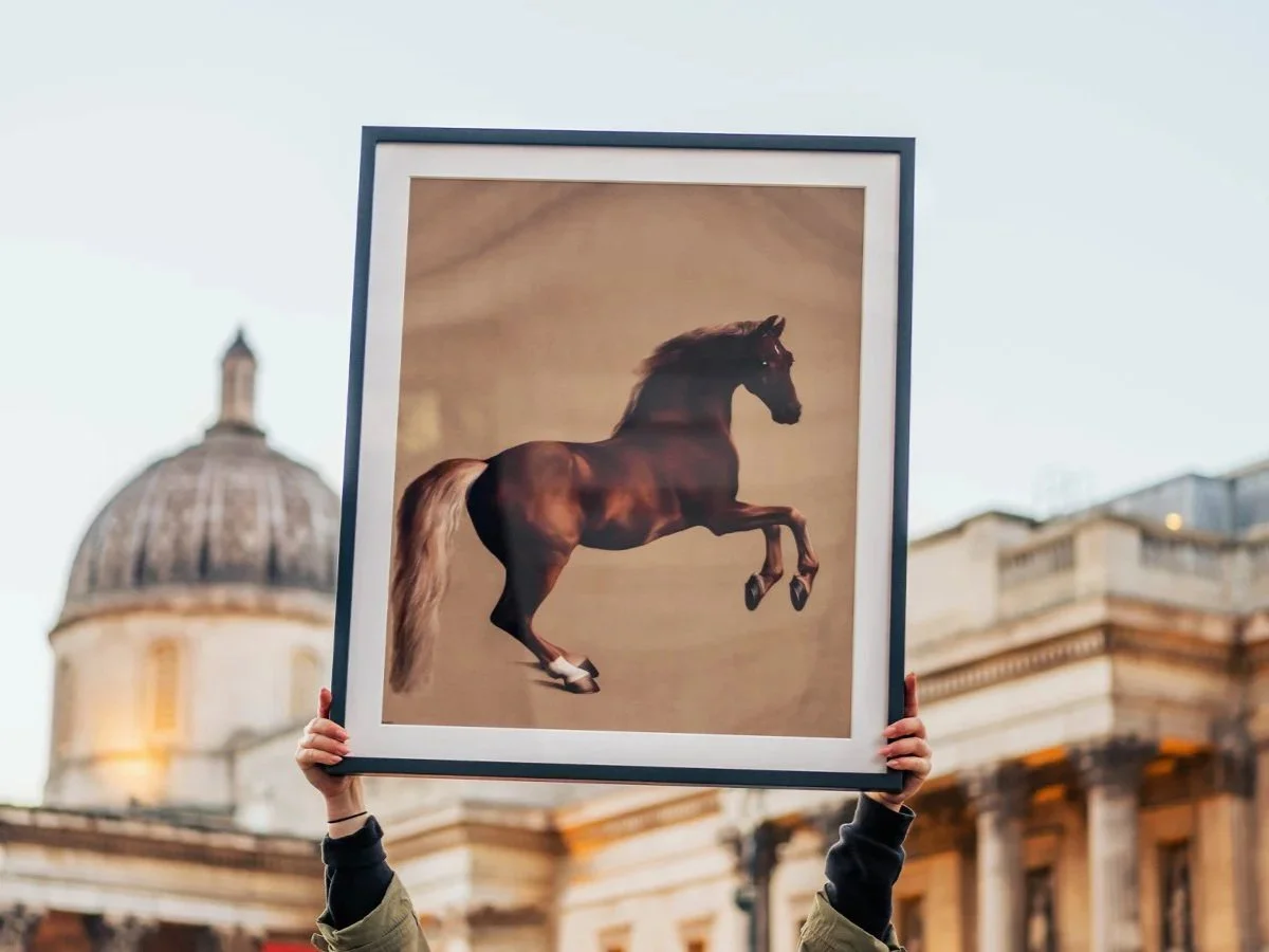 Person holding a framed painting of a horse jumping.