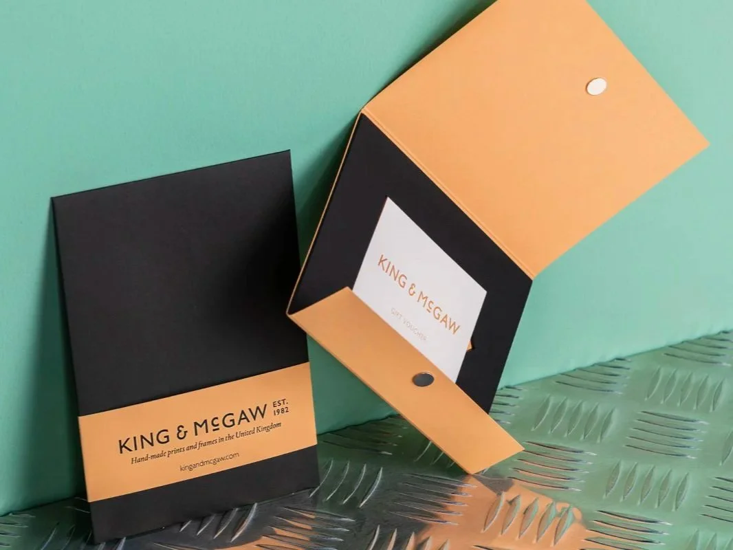 Open black folder with orange insert from King & McGaw, displaying the company logo and information, placed on a green surface with another closed folder nearby.