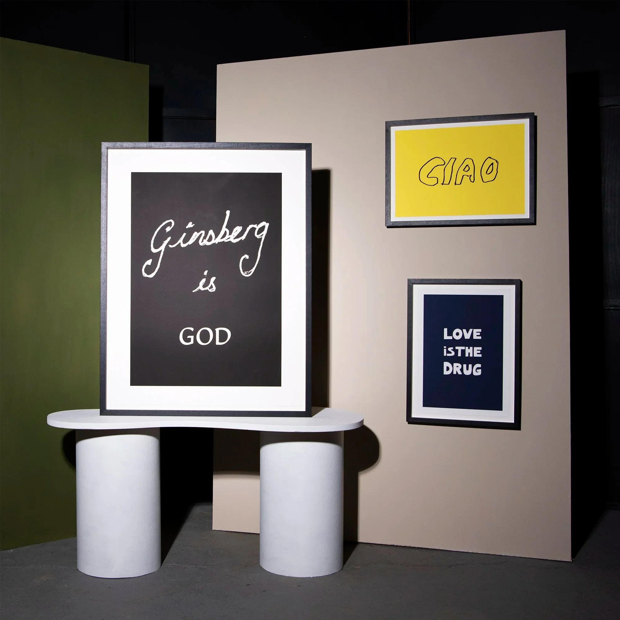 Dark-colored art display boards with handwritten text, supported by cylindrical white stands, set against a plain background with a partition wall.