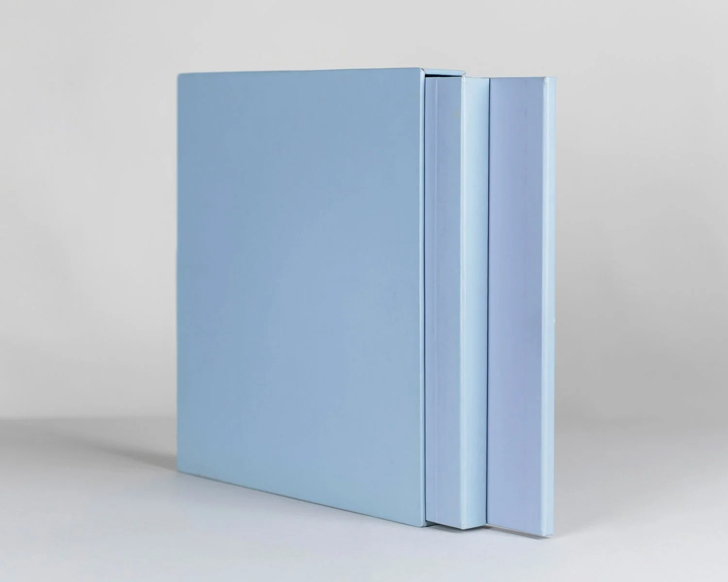 Three pastel-colored notebooks in shades of blue and purple standing upright on a plain white surface.