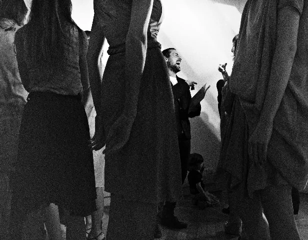 A group of people standing close together in conversation, with one person in the background laughing and talking.