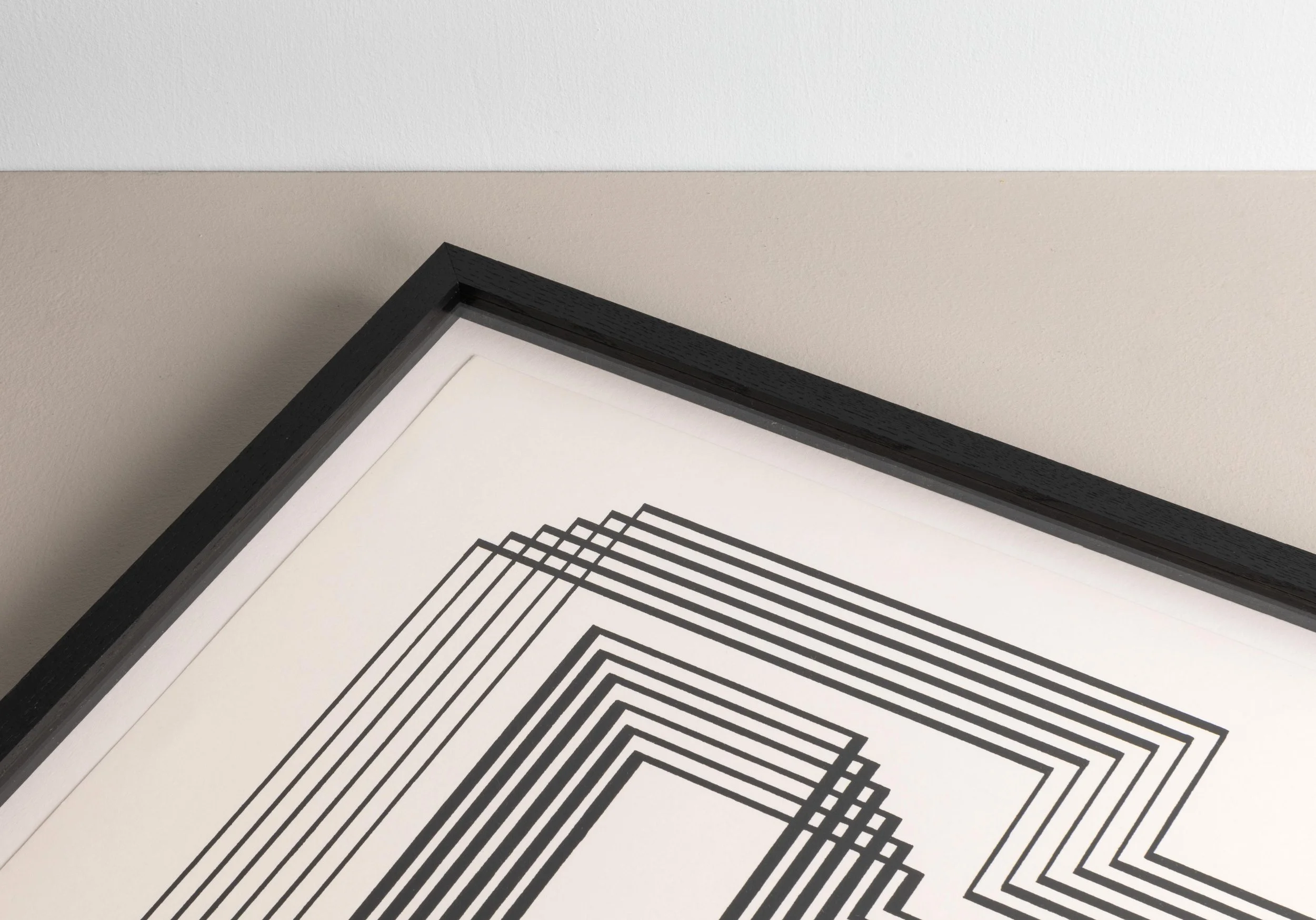 Close-up of a framed geometric black and white artwork on a white wall with a beige ceiling.