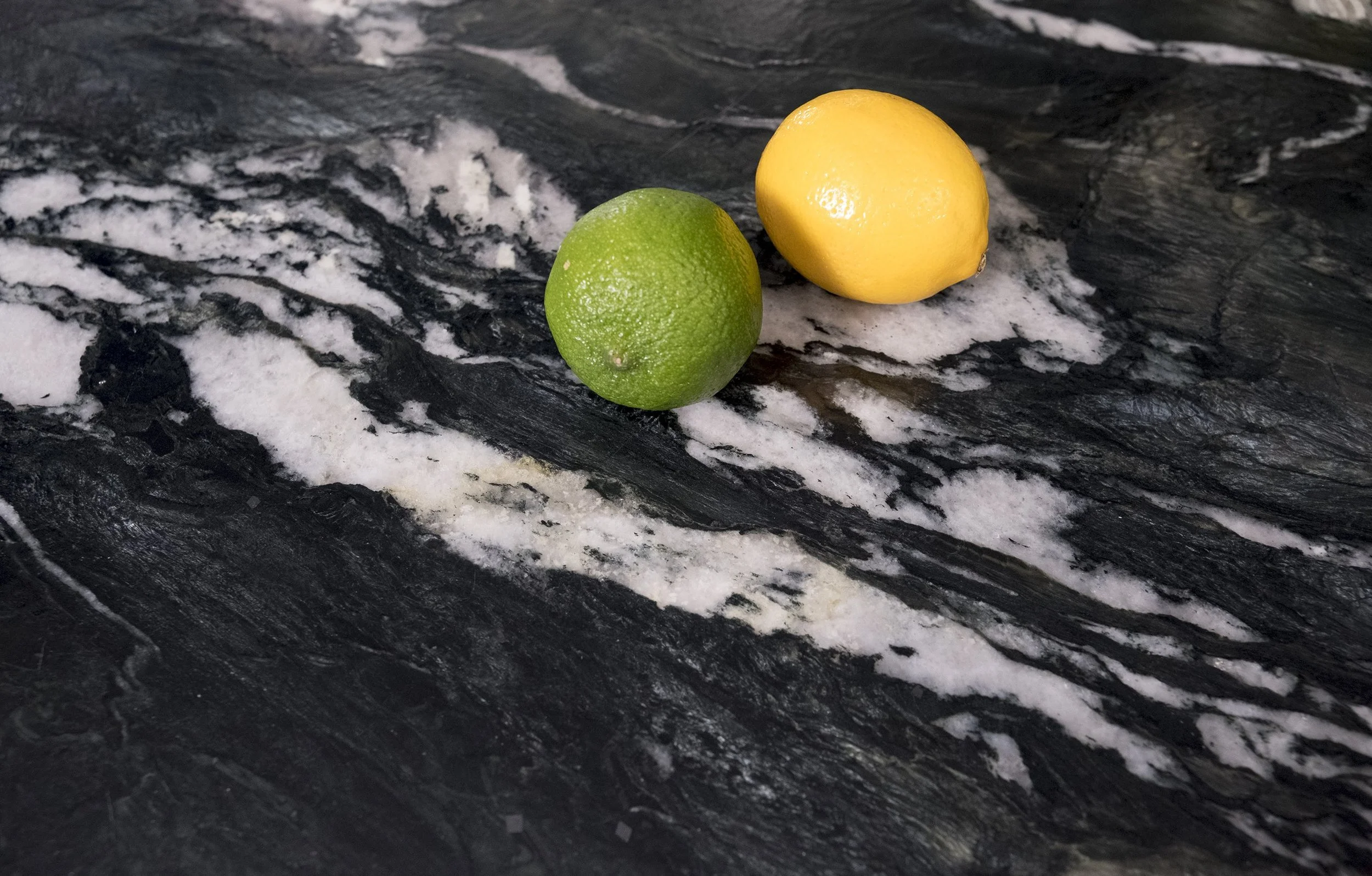 Closeup of black quartzite with marshmallow white flow throughout. Resting on top are a whole lemon and lime.