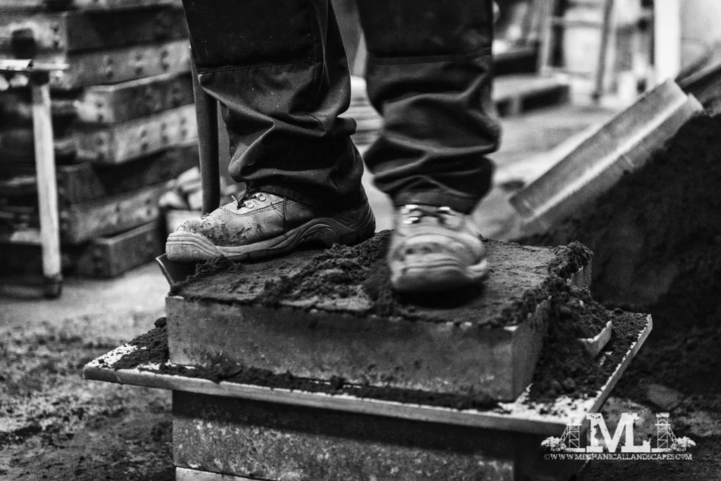 The only other person in the foundry was me, and I was taking photographs so there wasn't any opportunity to get one of people convesring, and almost all the pictures are of Keith in action, but this one uses a slowed shutter speed to capture the movement of Keith's boot as he tramples the sand into the box.