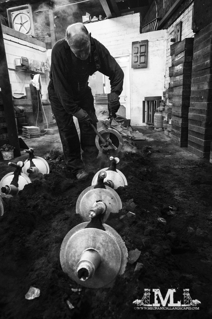 After being left to cool in the sand, a tap with a hammer releases the remaining sand and they are moved across the foundry into a pile ready for fettling.