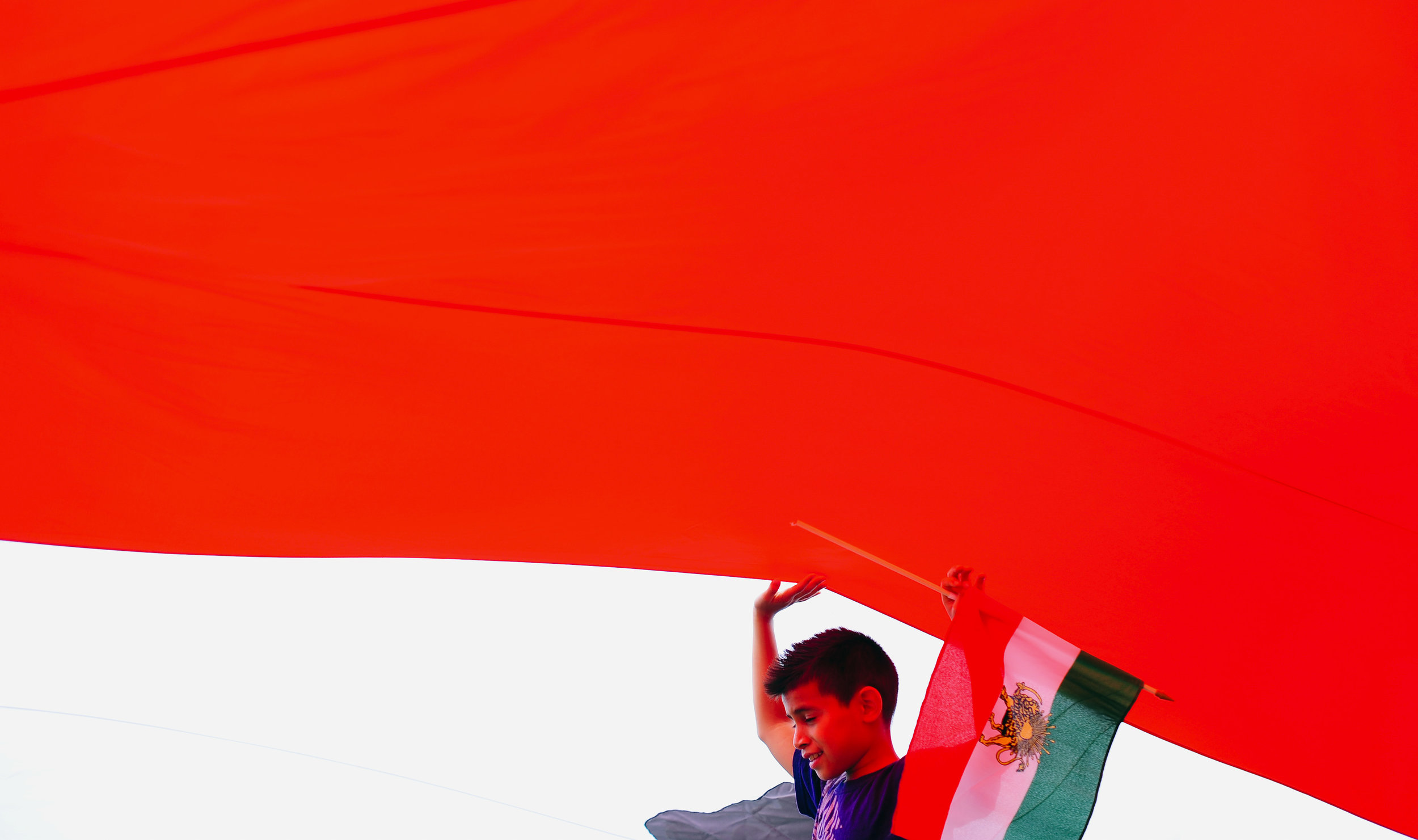  A boy walks under the flag of Iran used before the Islamic Revolution during the Persian Day Parade to celebrate the Iranian calendar New Year in New York. 