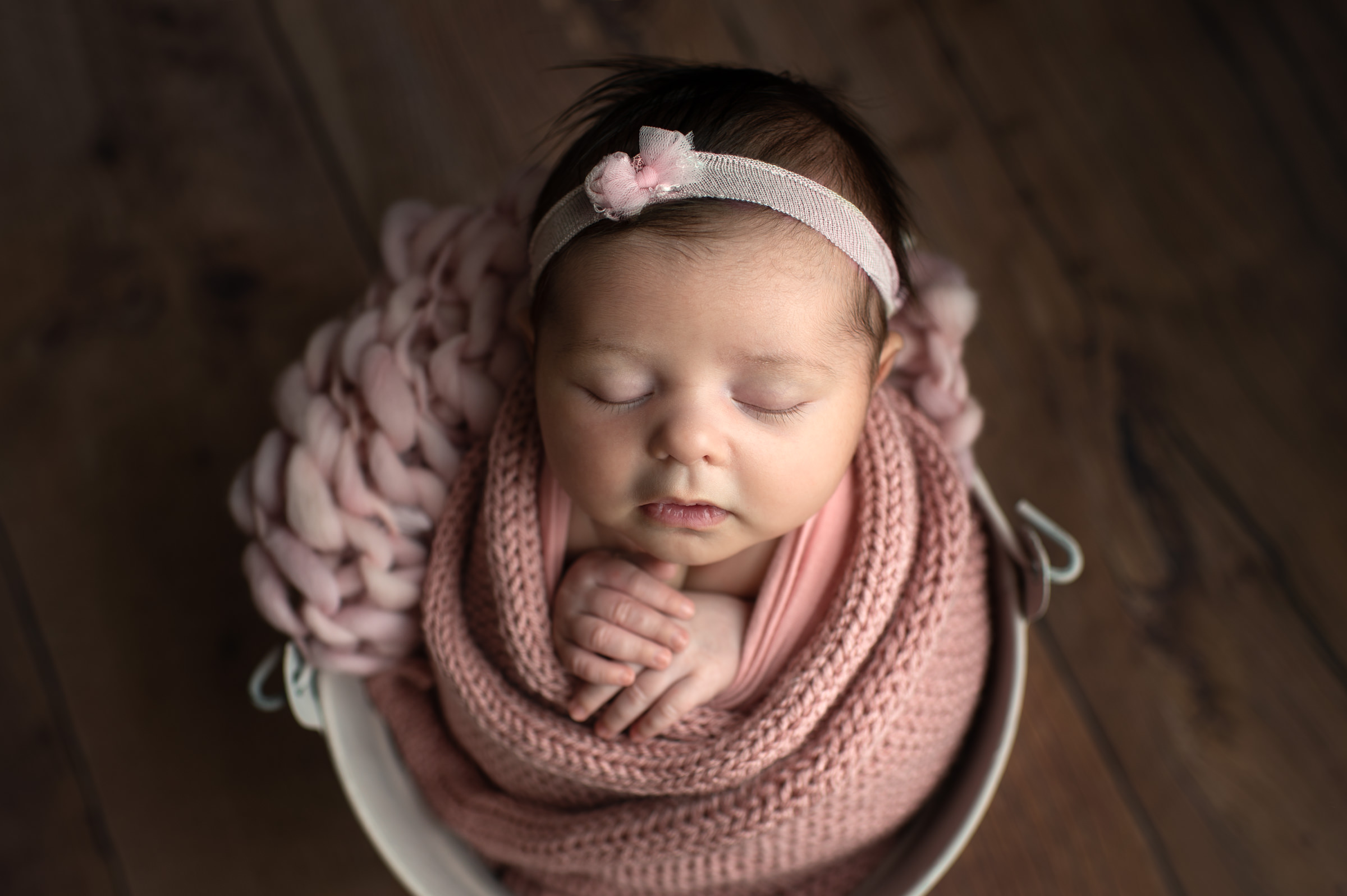 Sleeping newborn girl in a bucket wrapped in pink
