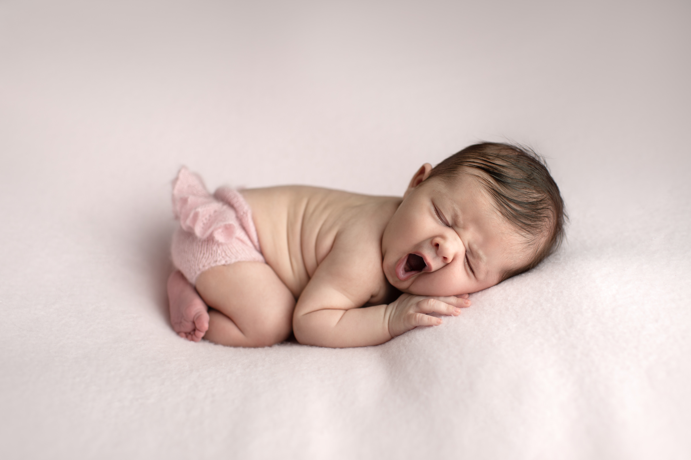 Yawning newborn girl on a pink blanket