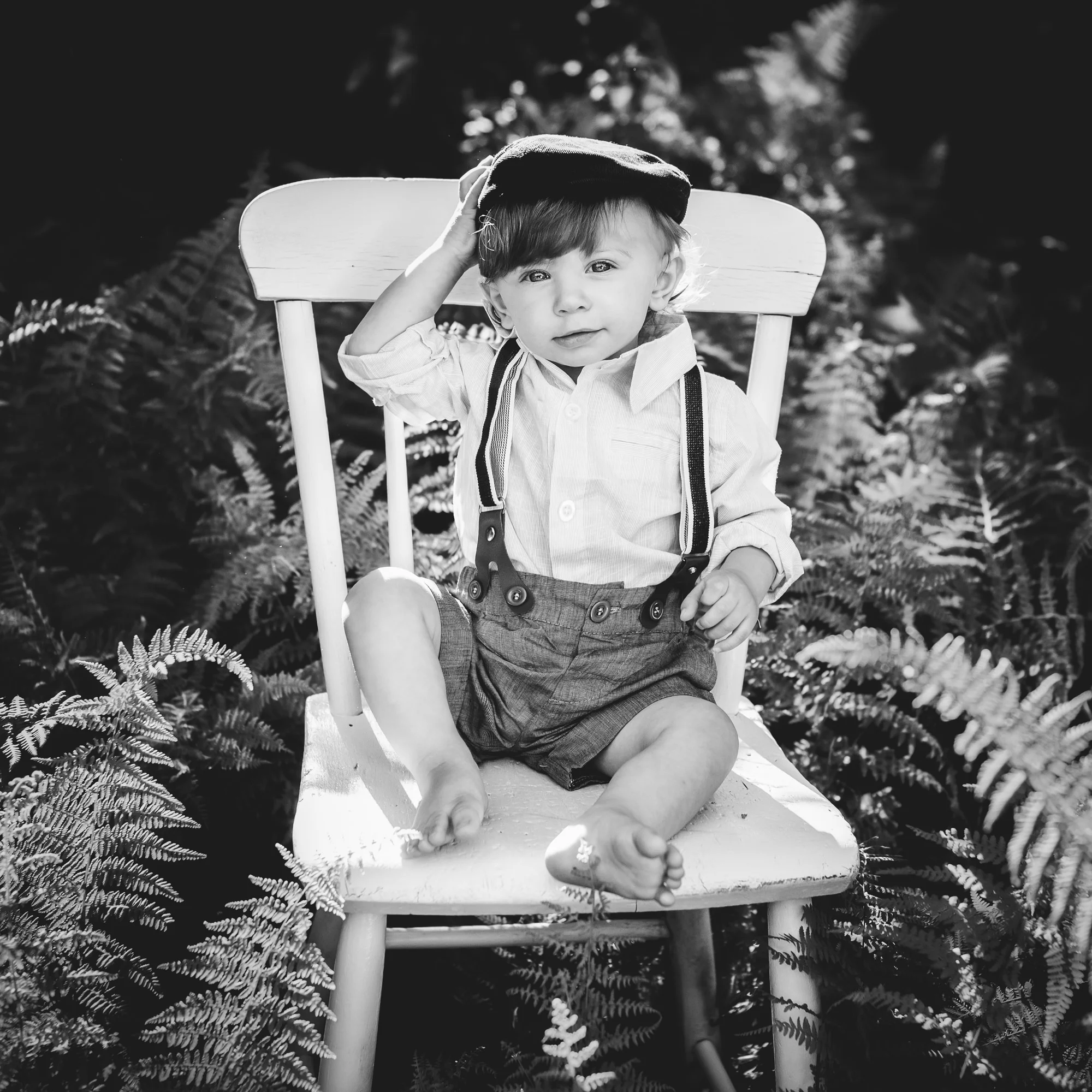 one year old boy sitting on a chair in the ferns outside in connecticut