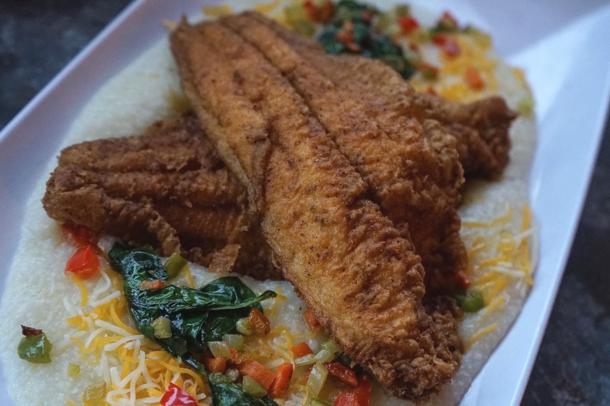 Boogaloo Grits served with Catfish. cheese. holy trinity. sautéed spinach. shrimp.