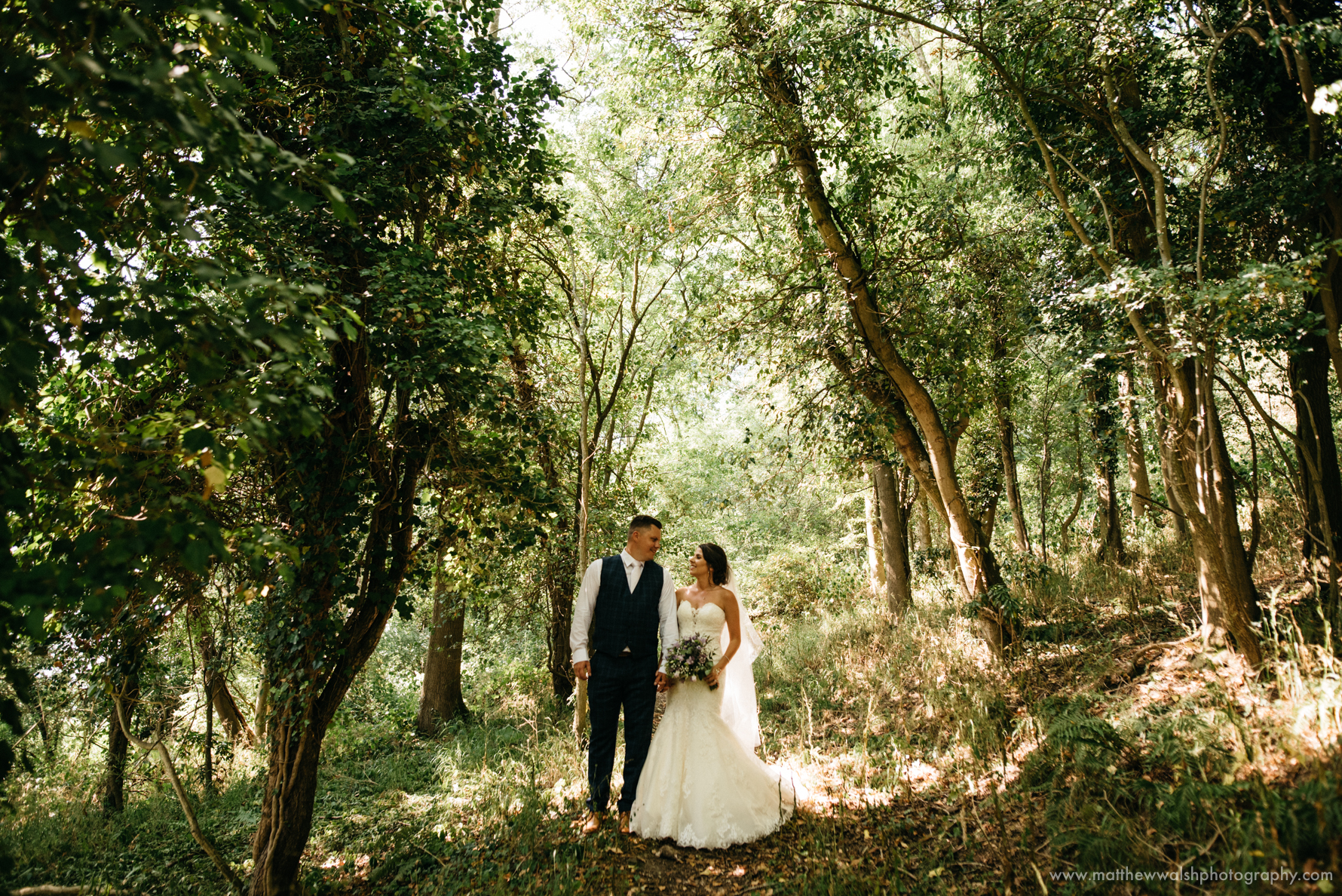 Touching moment as the new husband and wife stand under the artistic dappled light of the trees