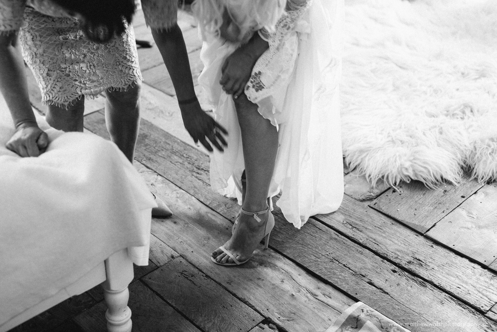 A black and white image of the bride putting her wedding shoes on