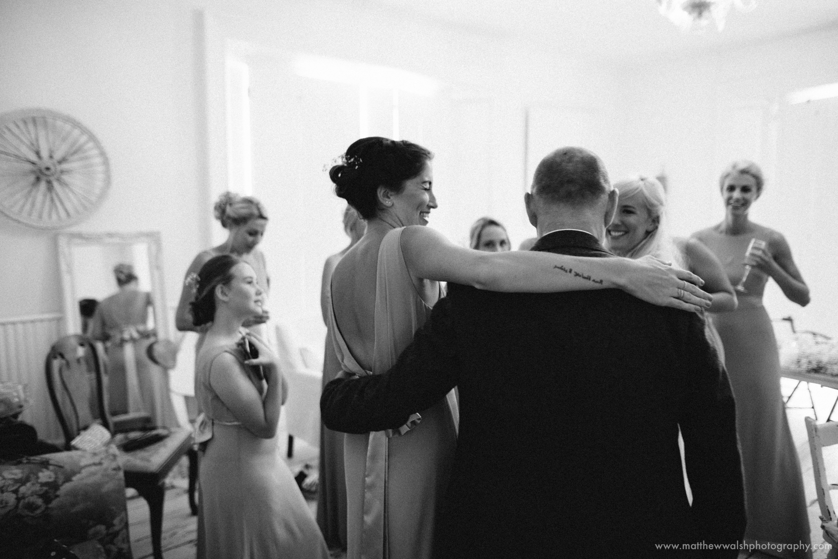 Father of the bride is welcomed into the room by the bride and bridesmaids