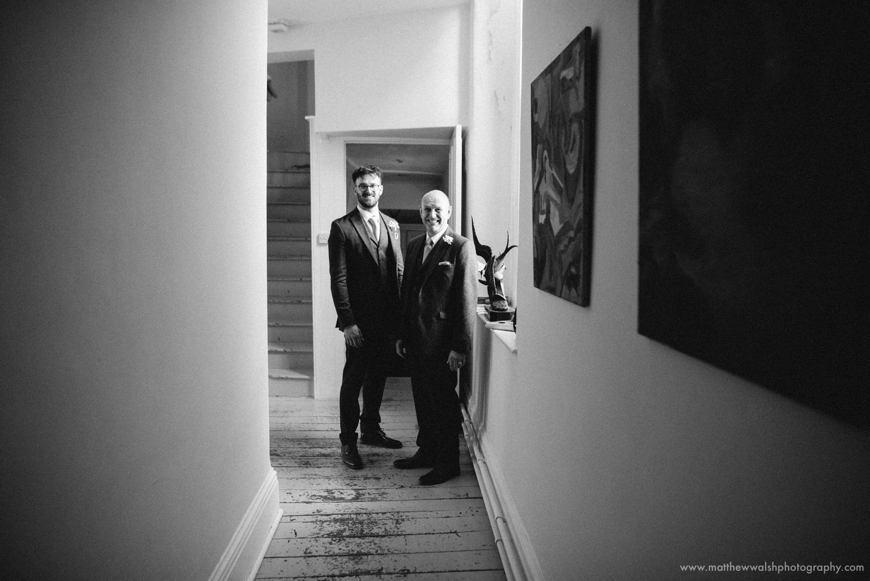 Father of the bride and brother pose for a picture together in the hallway of the main house