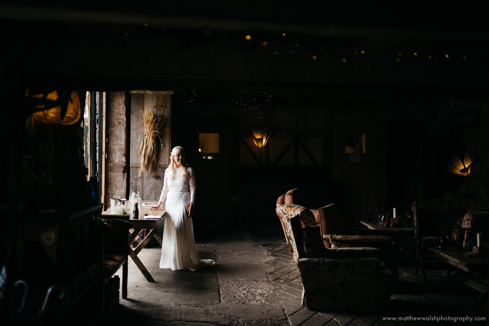 An observed moment of the bride standing by the barn entrance soaked in natural light in a perfectly exposed photograph
