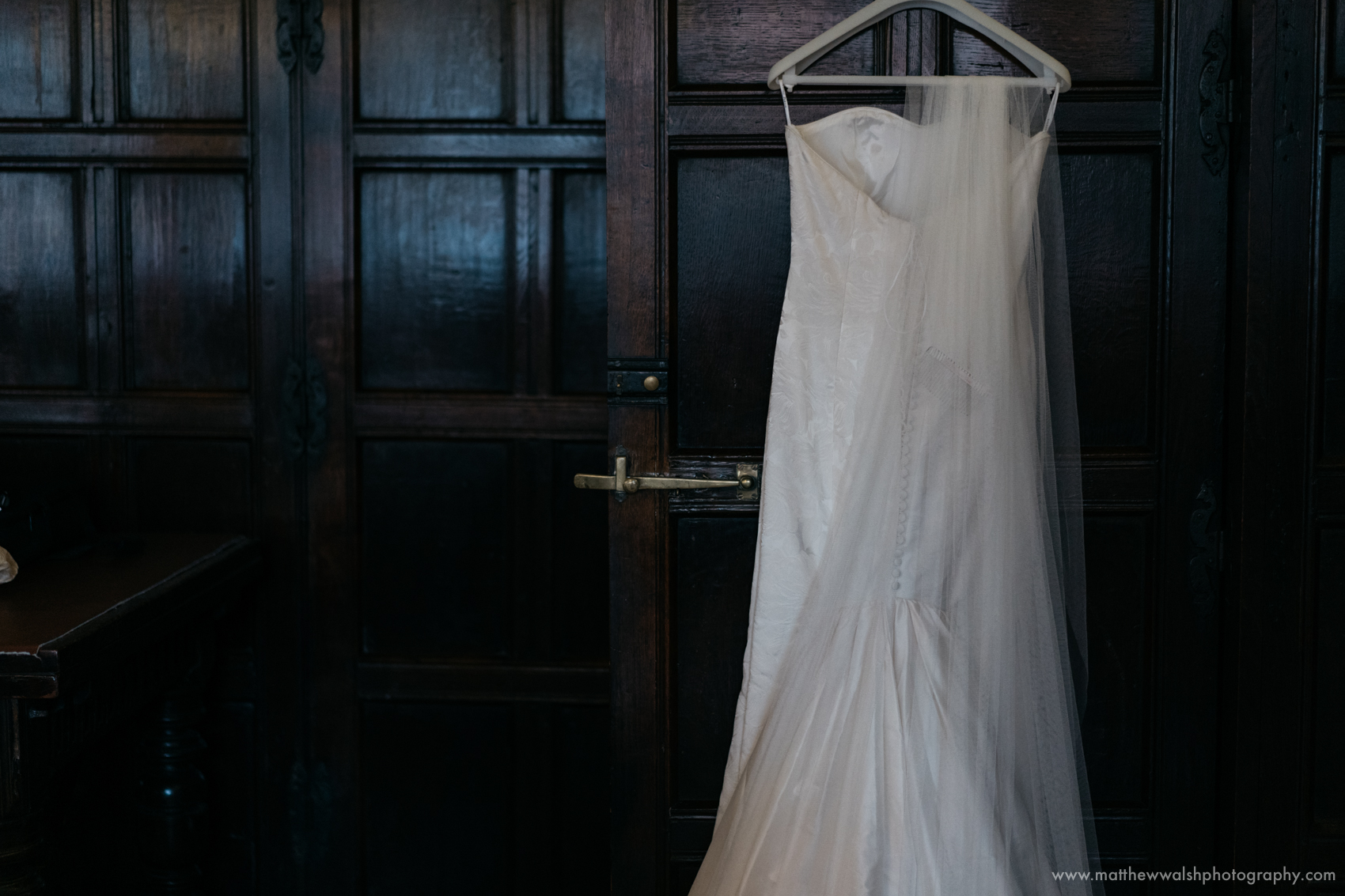 The wedding dress hanging from the door with a backdrop of natural wood panelled walls
