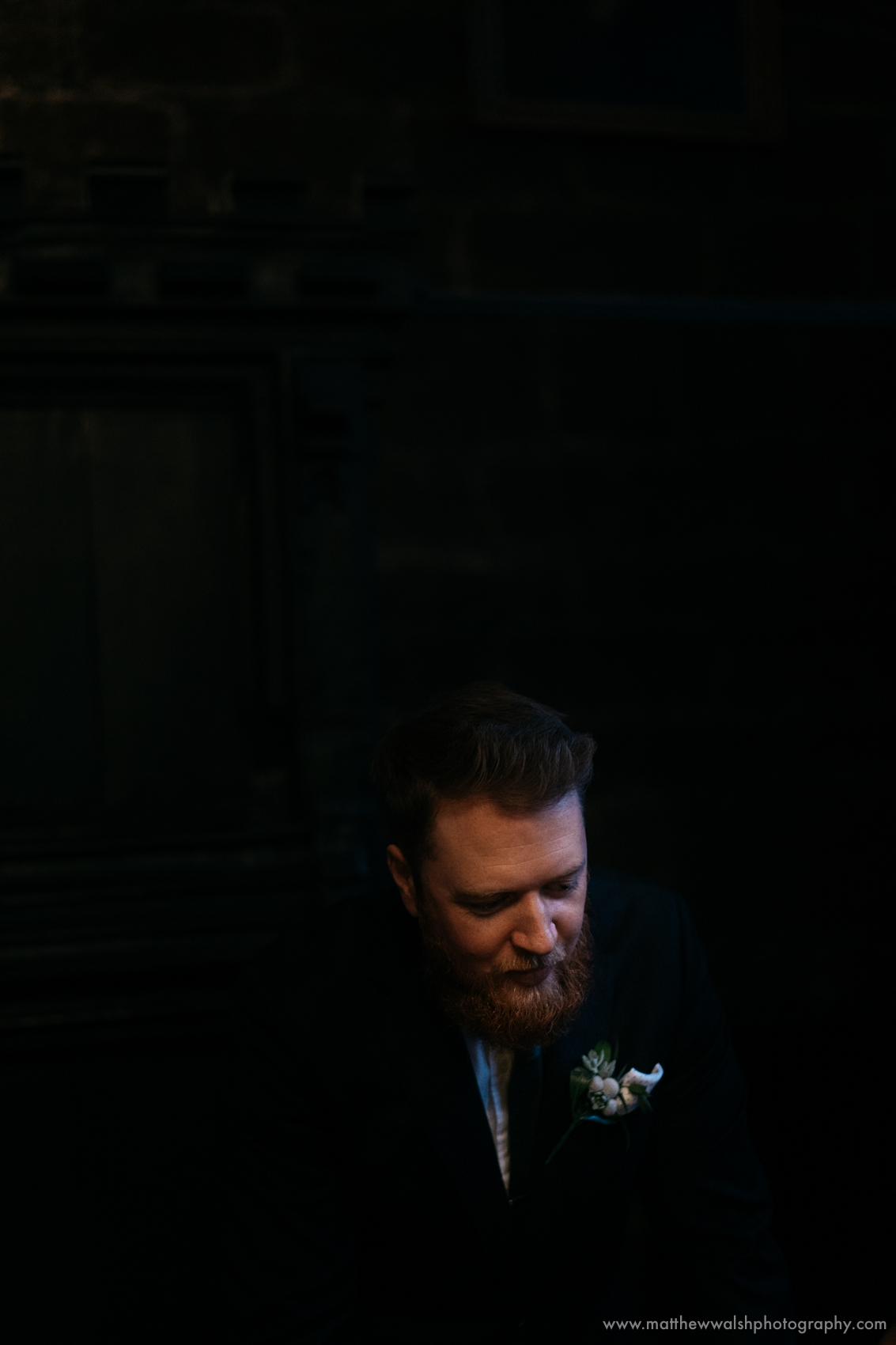 The groom making his final preparations in the dark light of the wedding venue