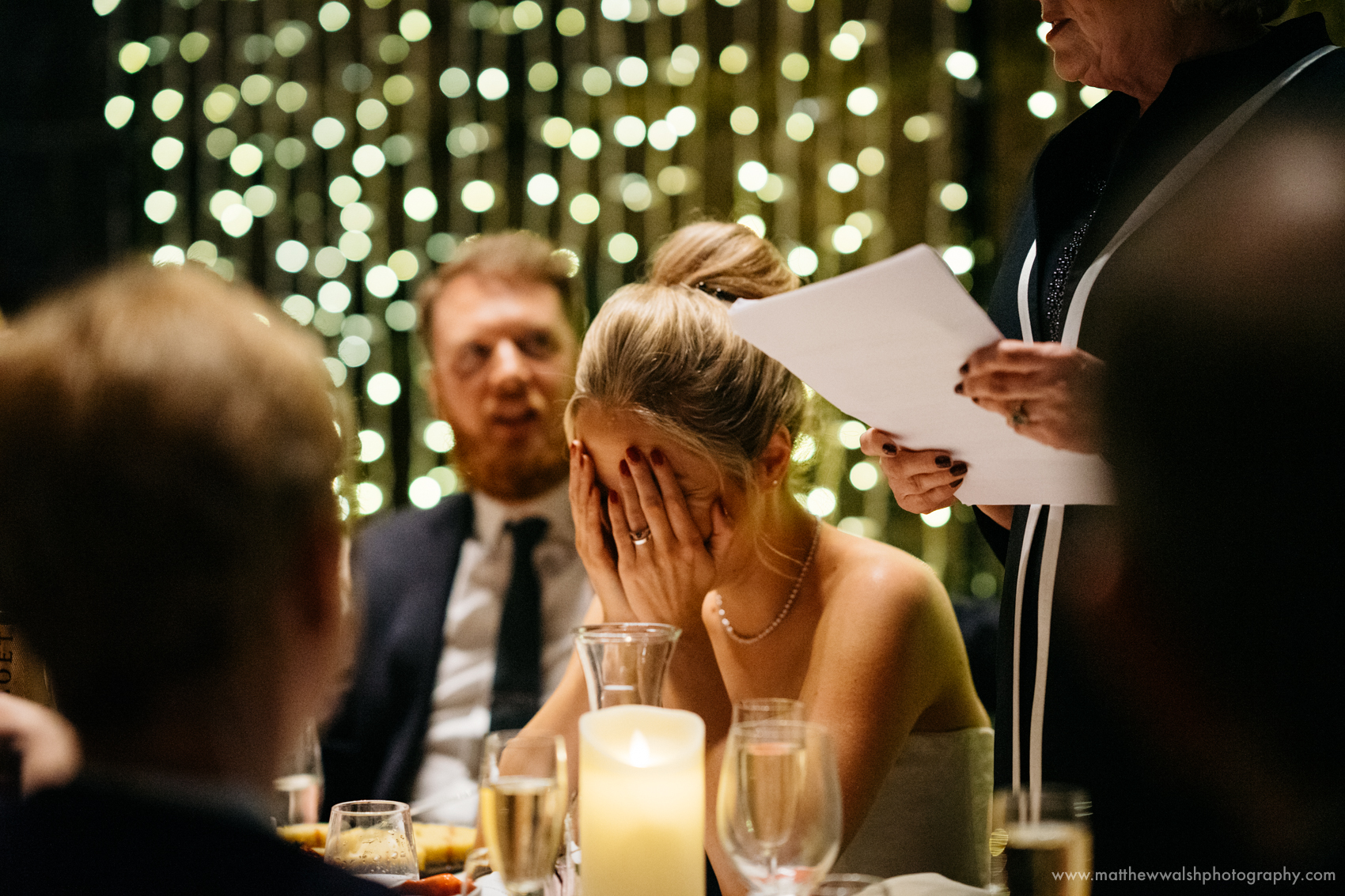 An embarrassed bride holds her head as the mother of the bride makes a speech