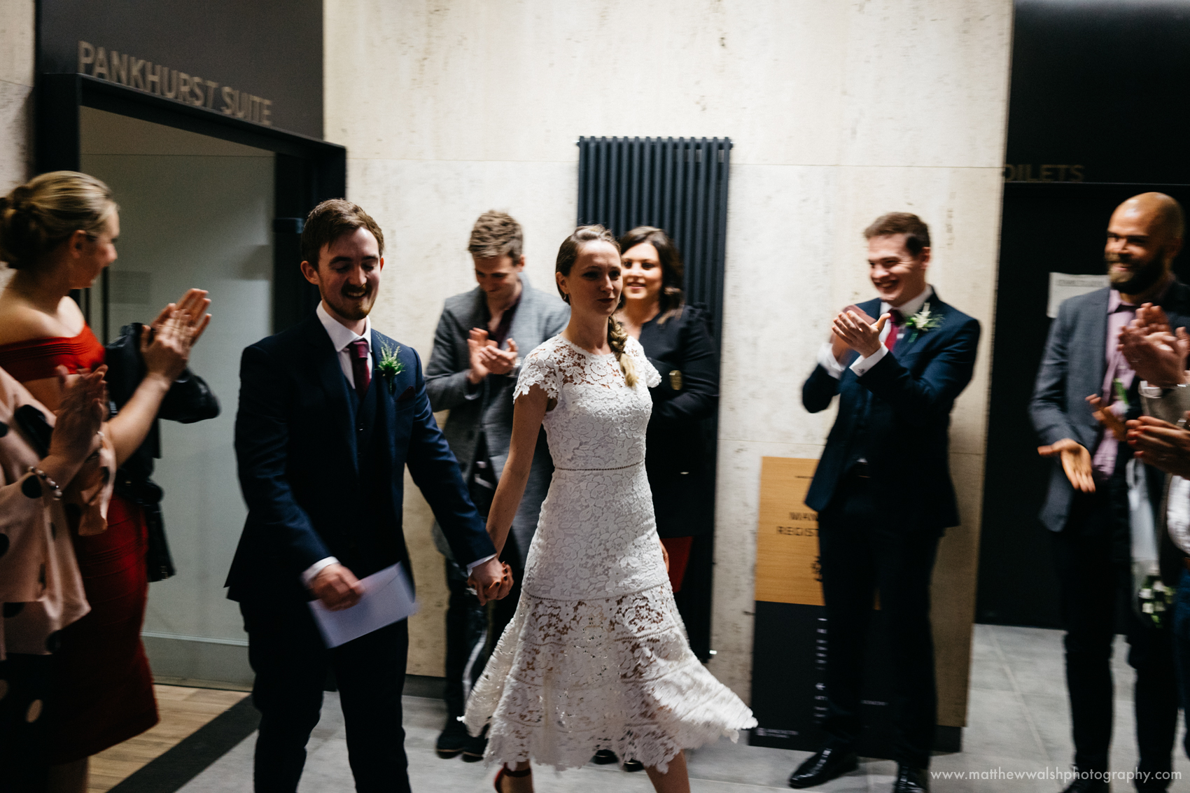 The bride and groom walk out of the ceremony venue to be met by their close friends and family