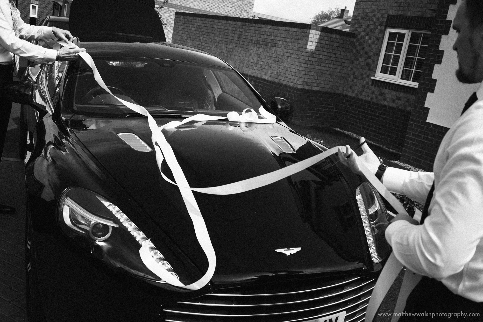 The father of the bride and a friend putting the ribbon on the Wedding car, an Aston Martin