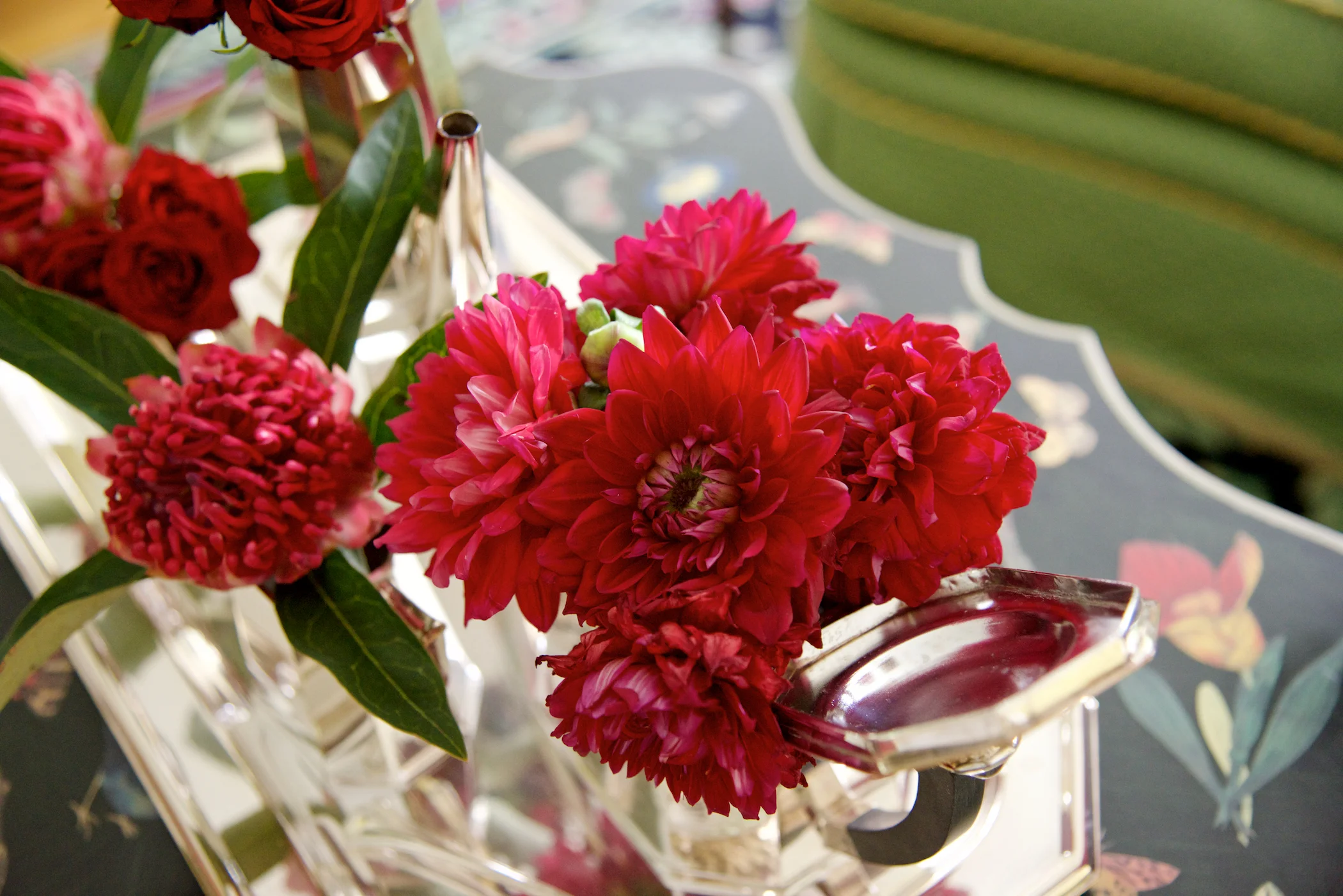 Red dahlias and roses adorn this silver tea set