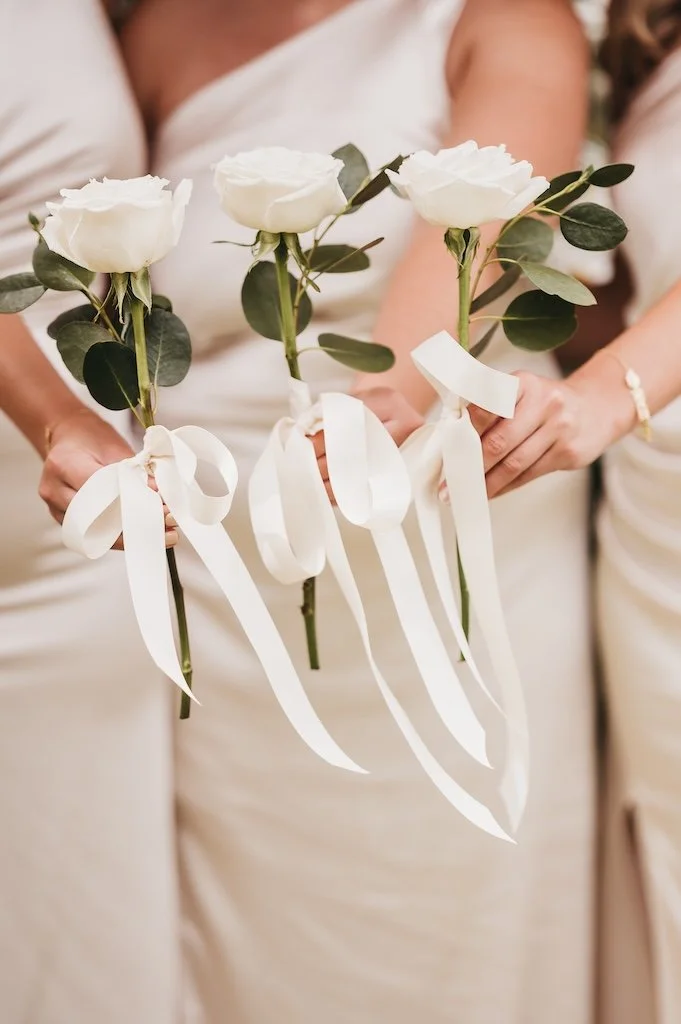 Bridesmaids holding a single rose and foliage tied with ribbon