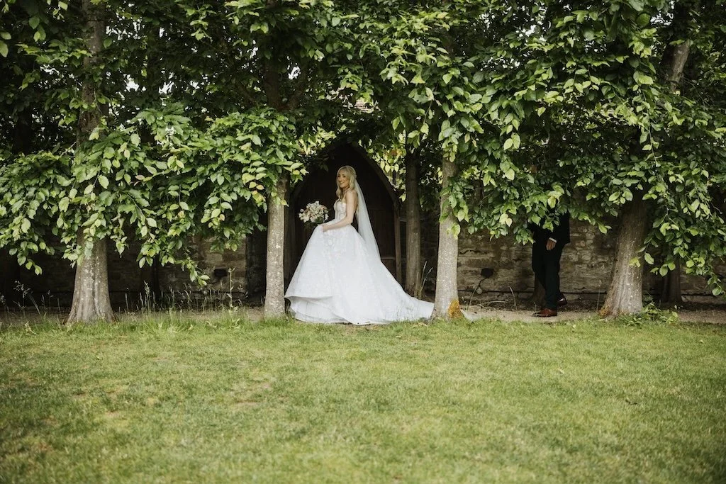 Bride walking between trees holding a bouquet by The Flower Story