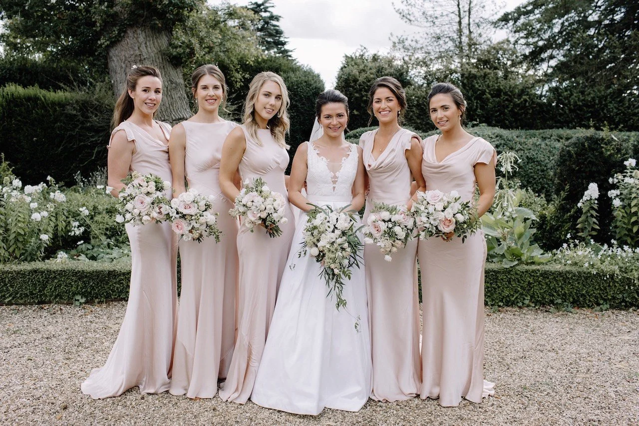 Row of bridesmaids carrying white and blush wedding bouquets at Kelmarsh Hall by The Flower Story