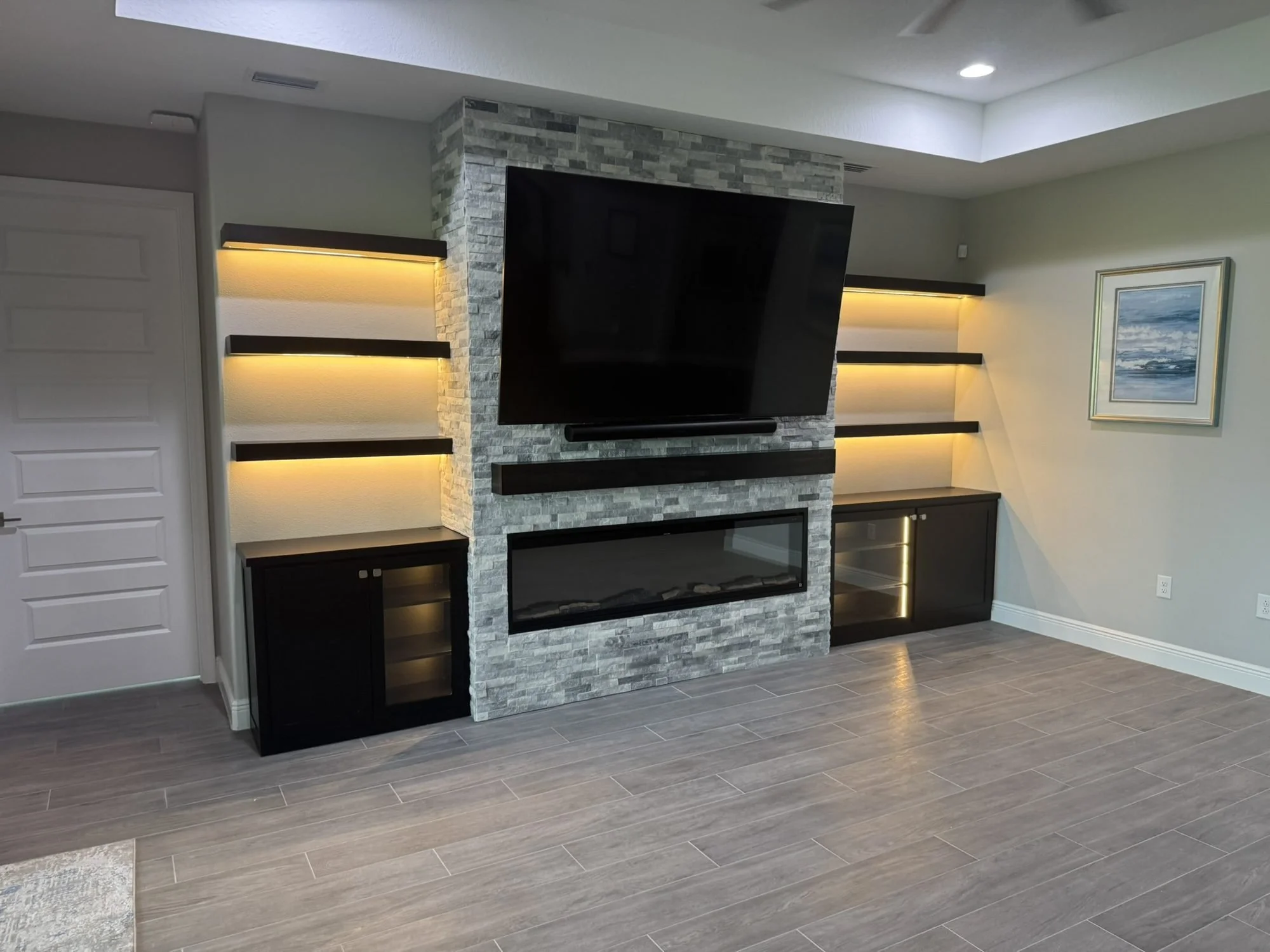 Media wall with stacked-stone fireplace surround and lit floating shelves