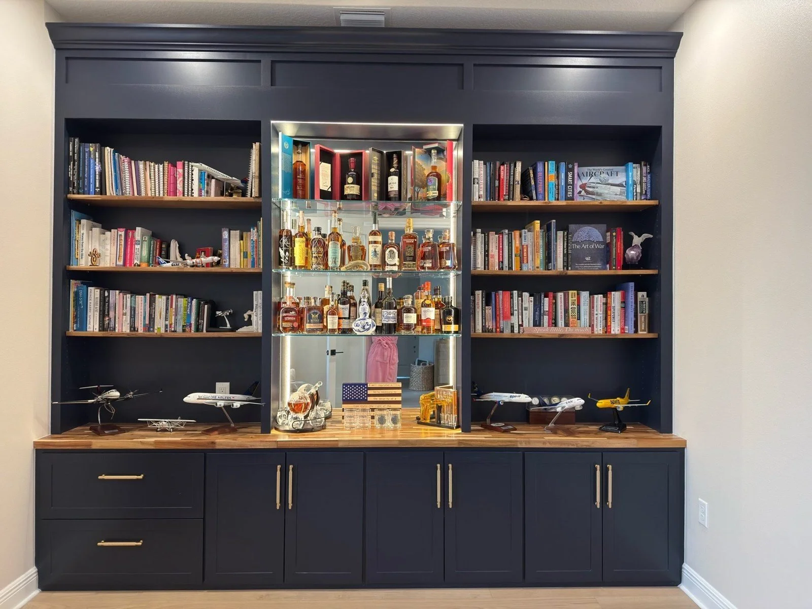 Navy built-in wall unit with bookshelves and lit mirrored bar