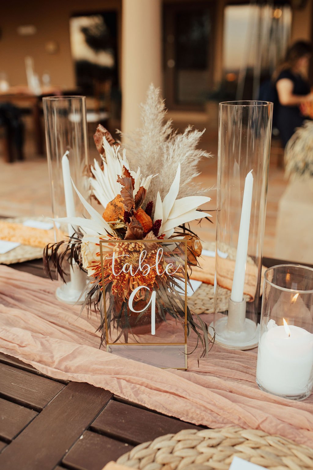 table number nine white text on clear acrylic sign on table with boho red and orange flowers behind and candles