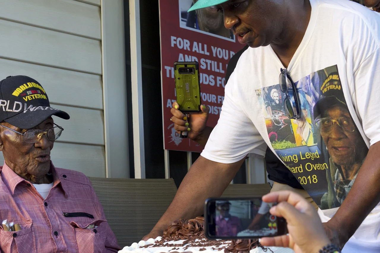 As celebrating Austinites look on from the front yard, longtime friend and caregiver Martin Wilford presents Richard Overton with his 112th birthday cake on Friday, May 11, 2018, at Overton’s East Austin home.