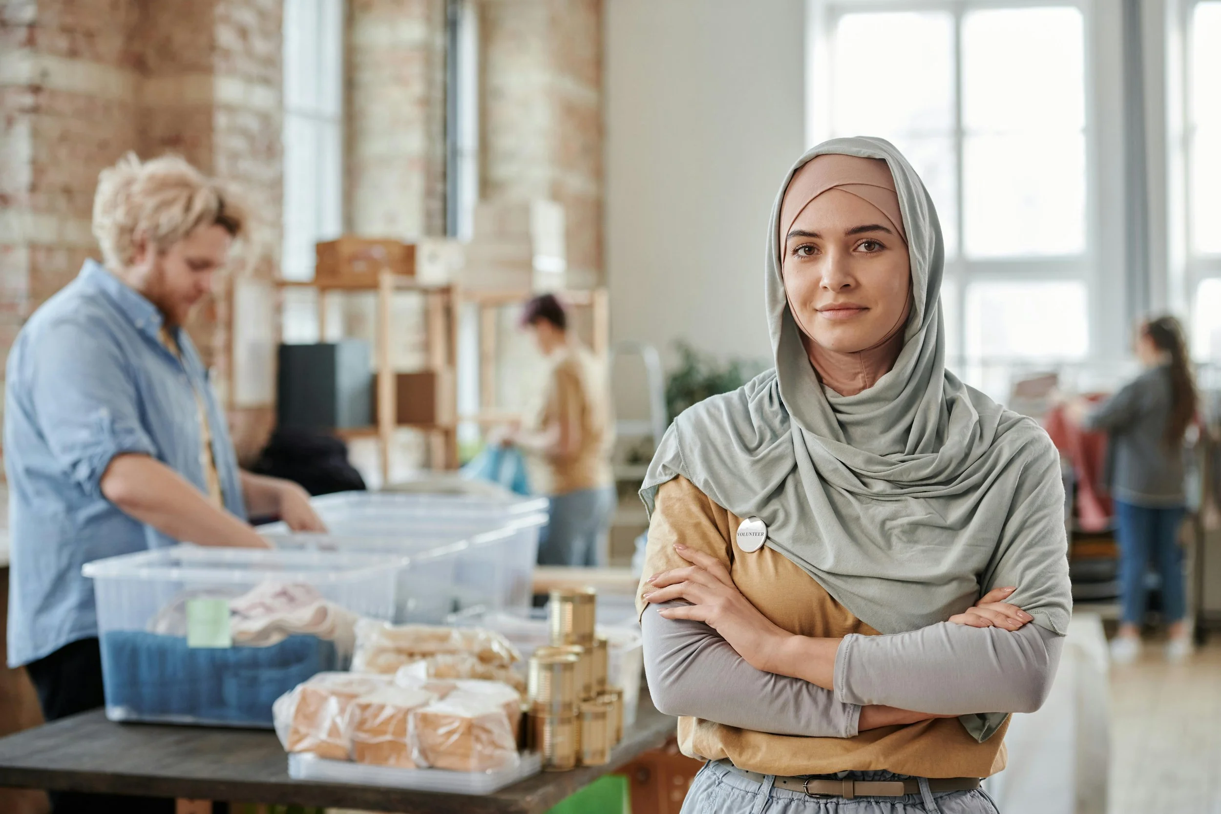 Lady wearing a hijab smiles at the camera while workers work in the background.
