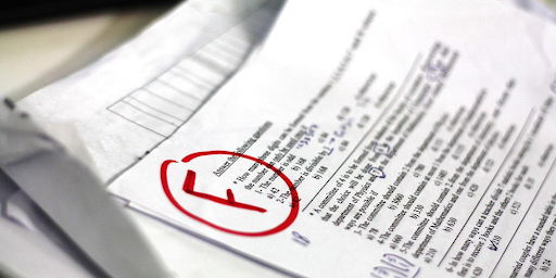 A close-up of a stack of test papers with one on top showing a red F grade.