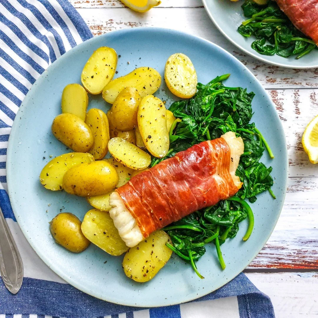 Plate of low FODMAP cod wrapped in Parma ham served with potatoes.