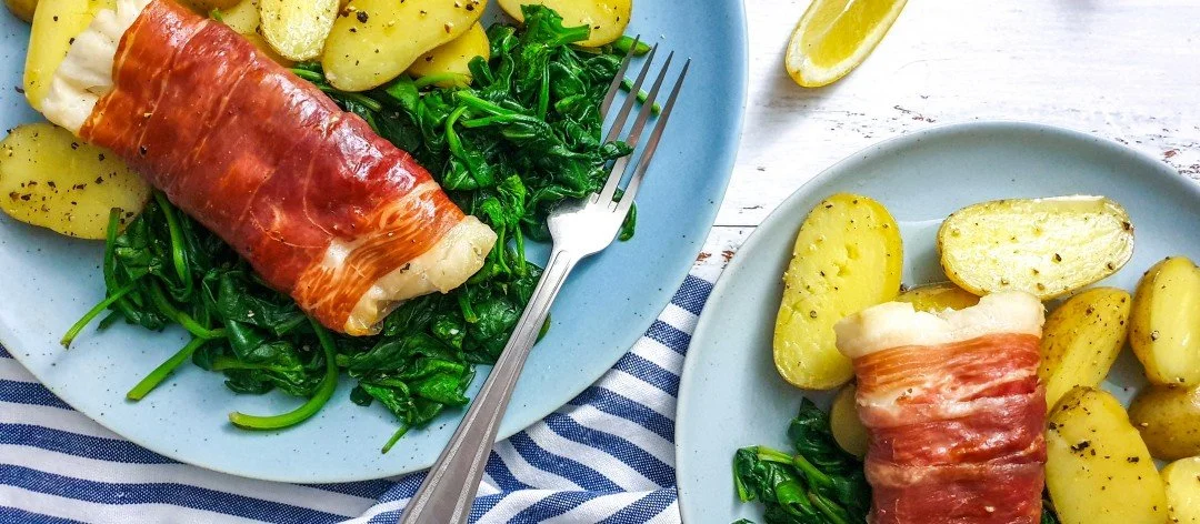 Plate of low FODMAP cod wrapped in Parma ham served with potatoes.