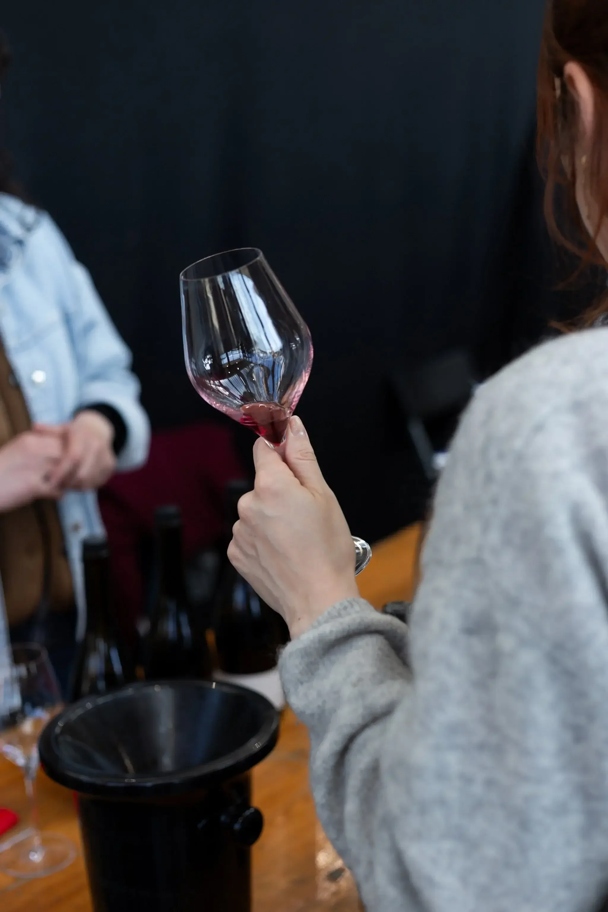 Une femme tenant un verre de vin rouge, en train de le goûter ou de l'observer, dans un environnement intérieur.