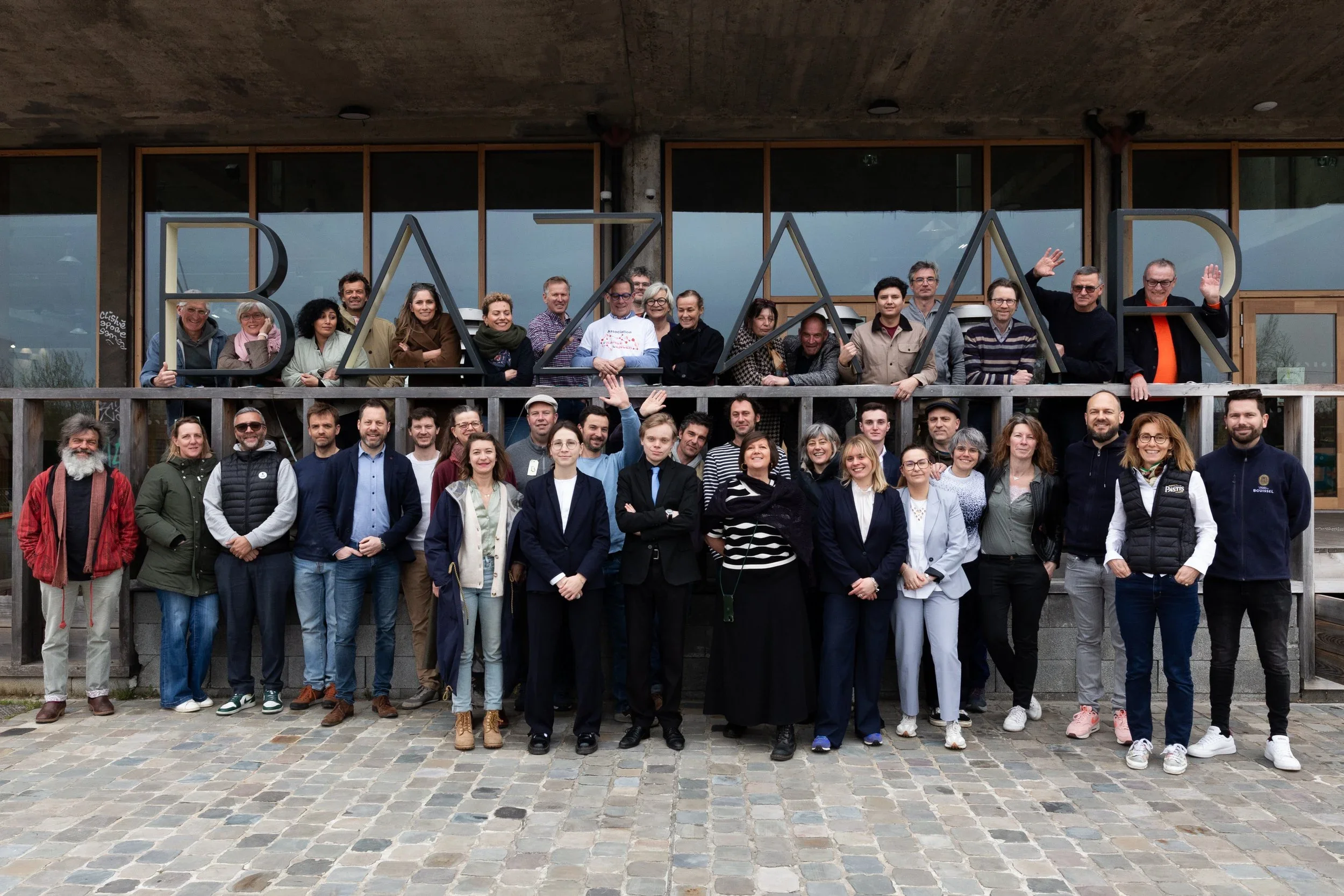 Une grande groupe de personnes posant devant un bâtiment avec une structure en bois et une grande inscription 'BATAAR' sur la façade. Il s'agit d'une photo de groupe lors d'un événement ou d'une rencontre.