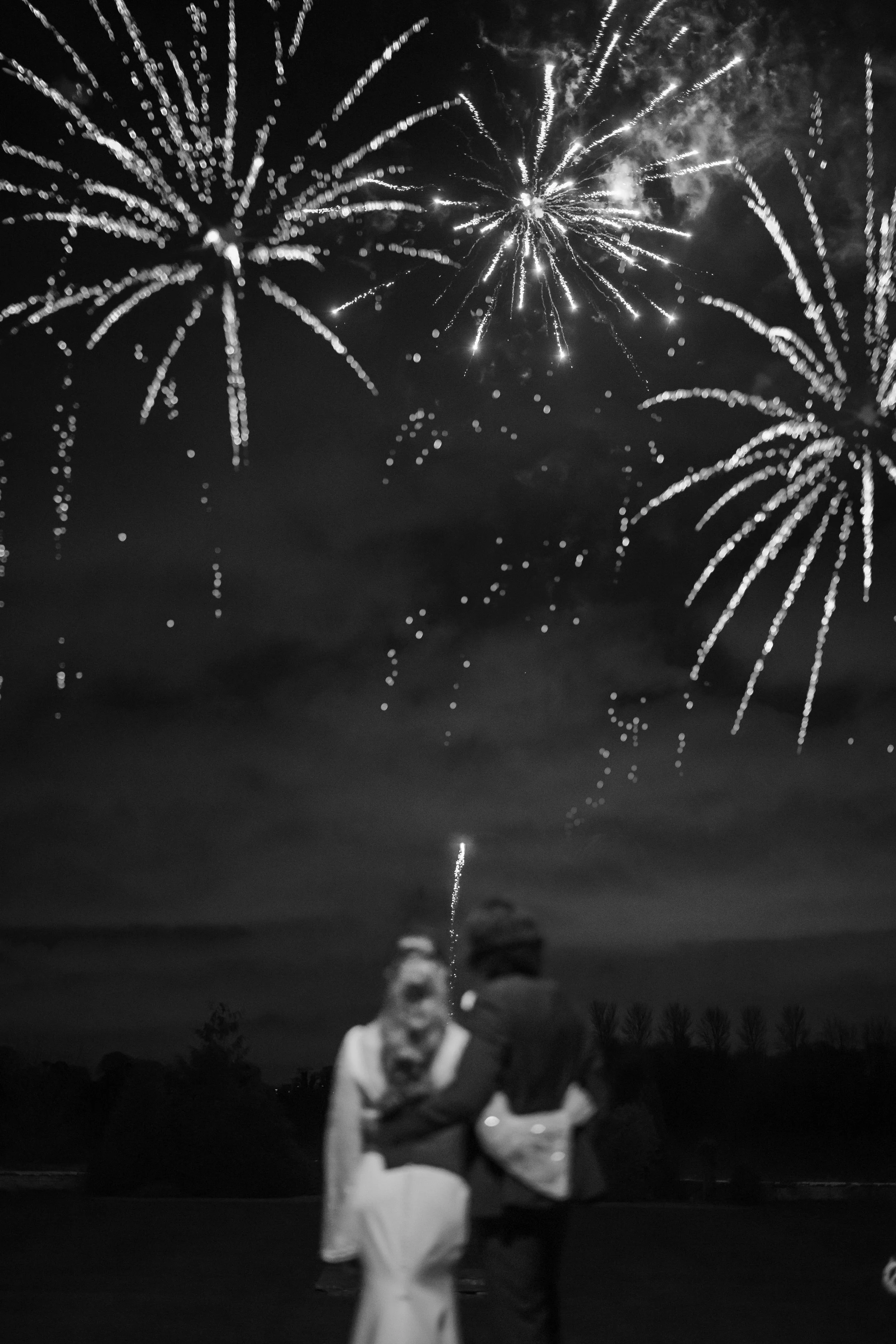 Bride and groom standing together as fireworks light up the sky on their wedding day