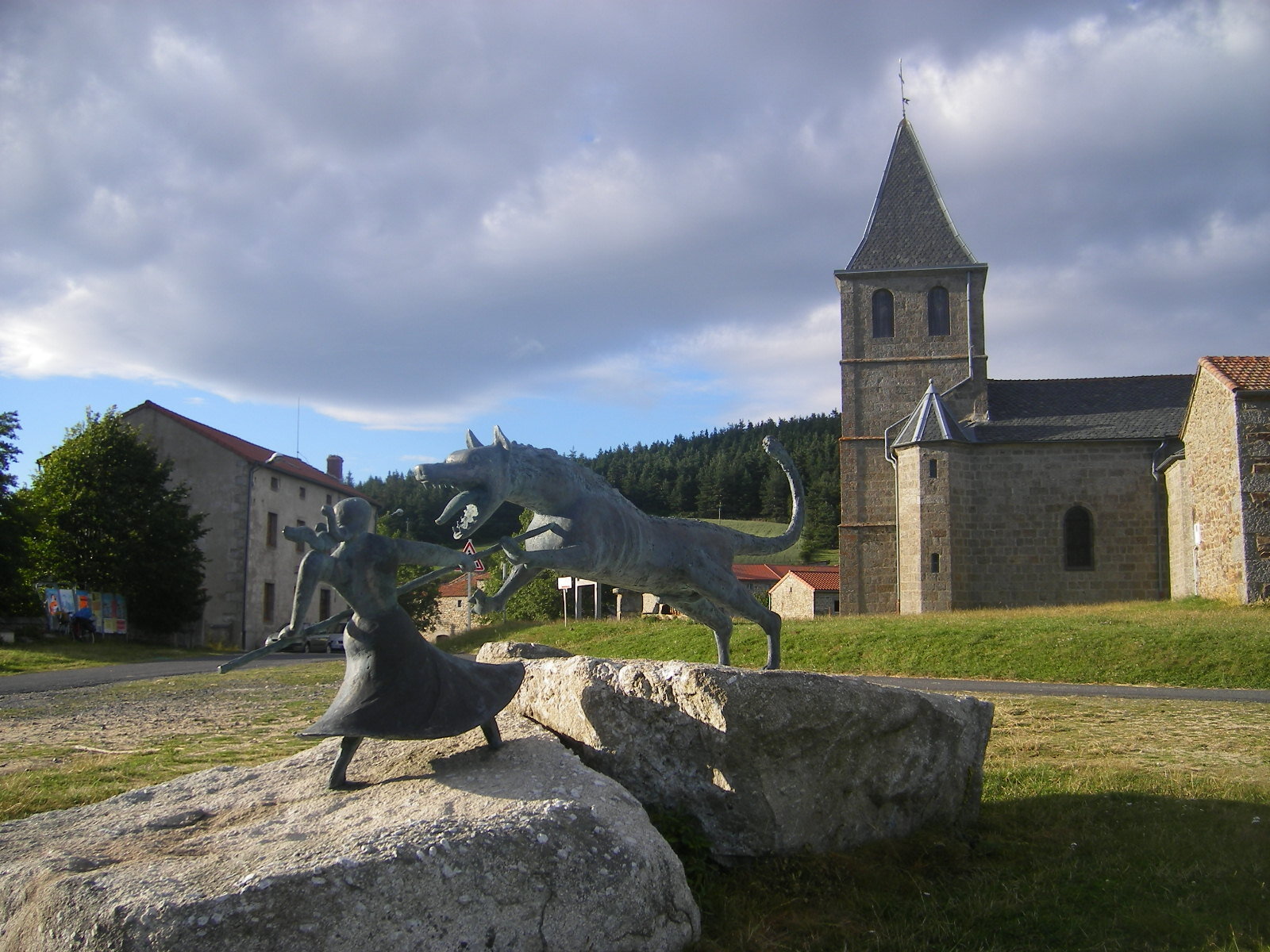  The battle of Marie-Jeanne Vallet, known as the "Maid of Gévaudan", against the beast. Sculpture by Philippe Kaeppelin, Auvers (Haute-Loire). Auvers, left: catholic church, right: municipality, center: monument of the Gévaudan beast. Photo by Szeder