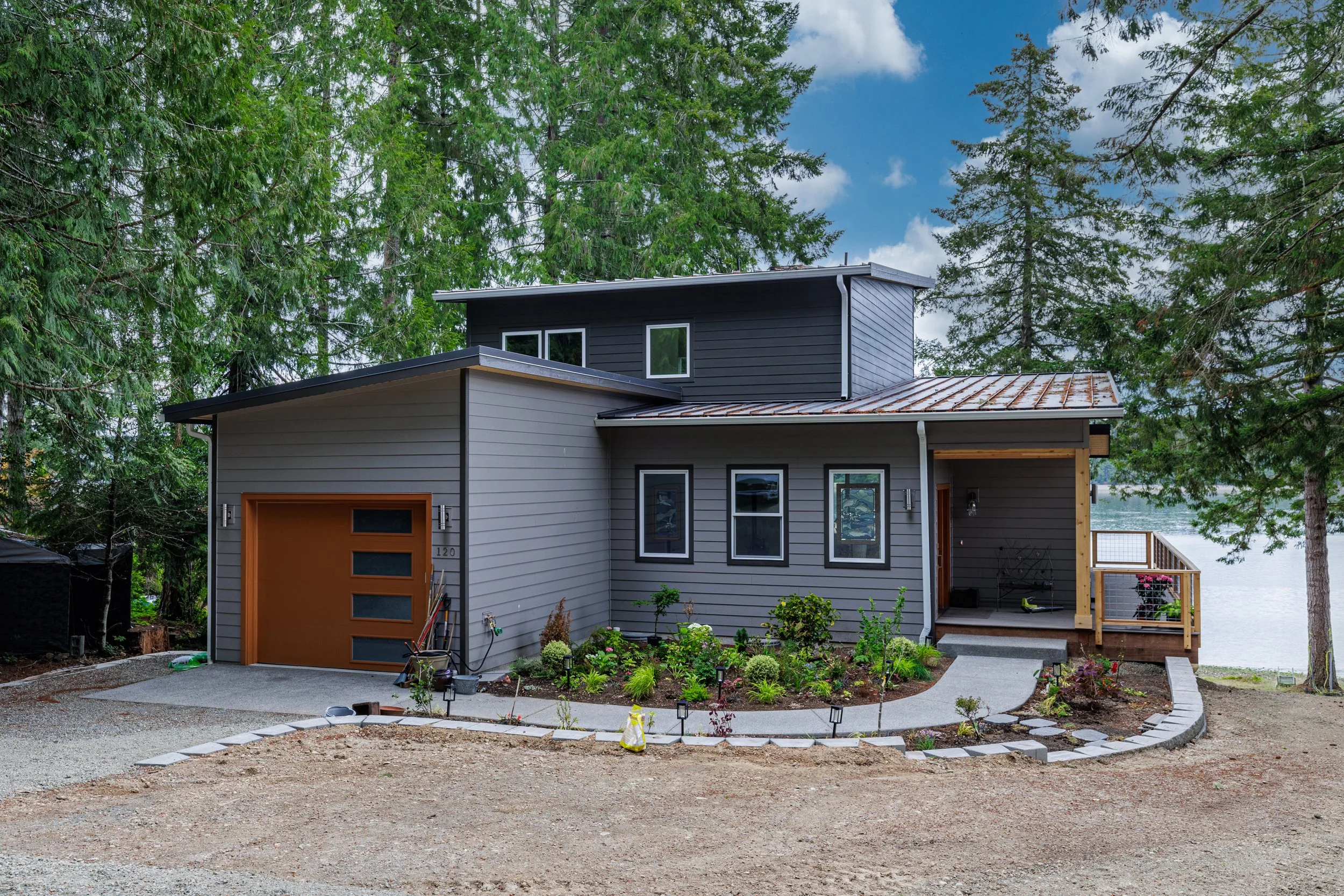 Front exterior of a custom waterfront home on Pickering Passage in Shelton, WA, featuring gray siding, a wood garage door, covered entry, metal roof, and waterfront setting - FoxHead Construction.