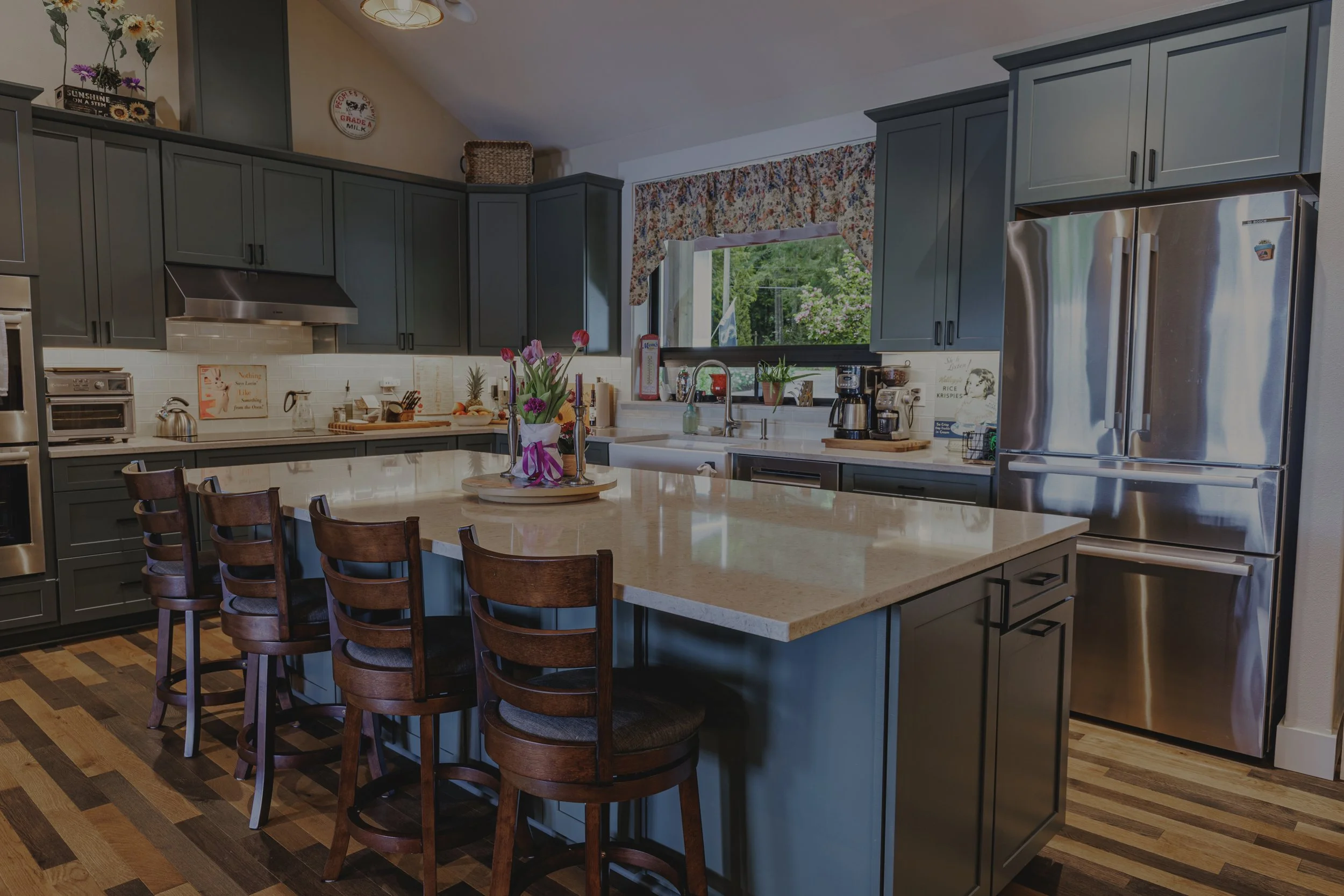 Custom kitchen in Amy and Phyllis’s Lake Limerick home in Shelton, WA, featuring sage green cabinetry, light stone-look countertops, stainless steel appliances, and island seating - FoxHead Construction.