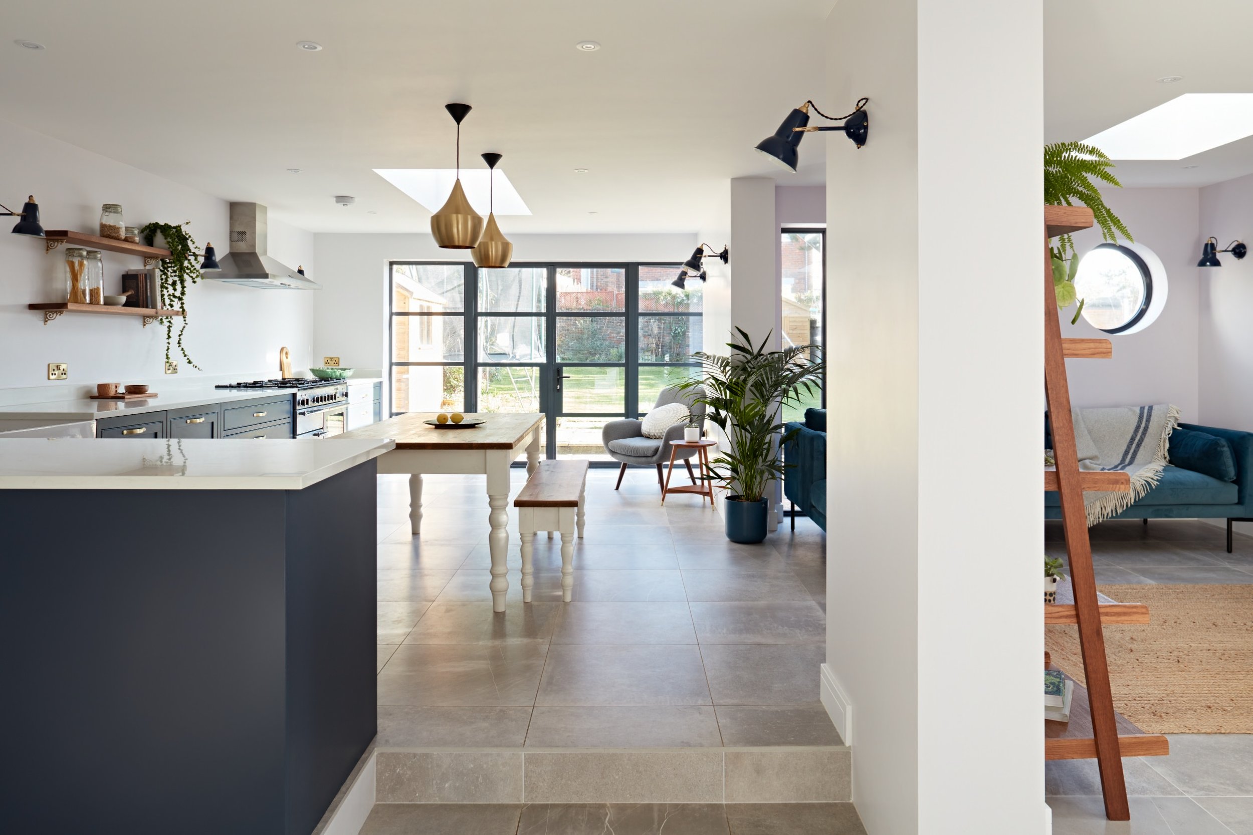 Open-concept modern kitchen and living room with large windows, plants, and contemporary decor.