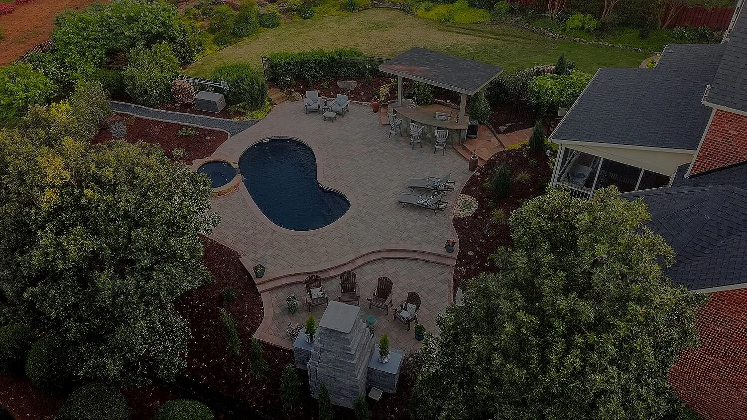 Drone image of paver patio, inground pool, outdoor kitchen with pavilion