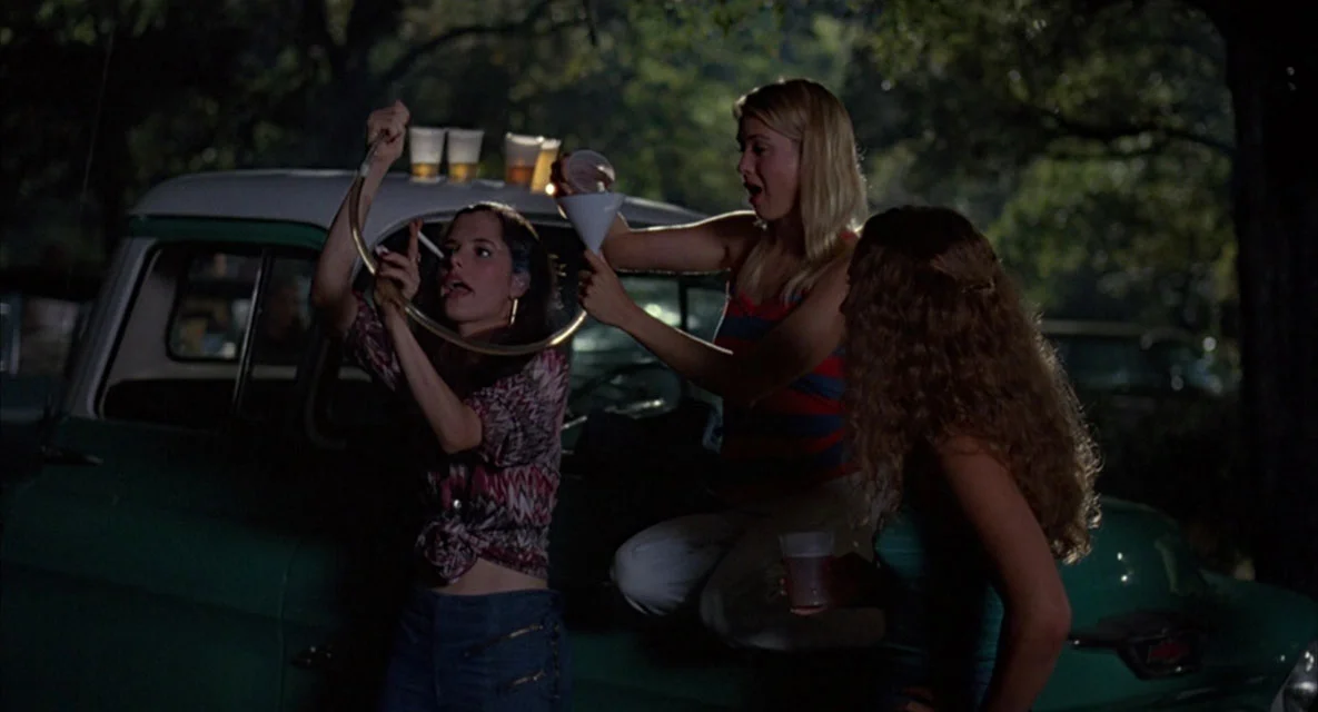 Darla (Parker Posey) gets ready to drink from a " beer bong " as a fellow student (an uncredited Renée Zellweger ) pours the beer during the "Party at the Moontower" © 1993 Universal City Studios, Inc.