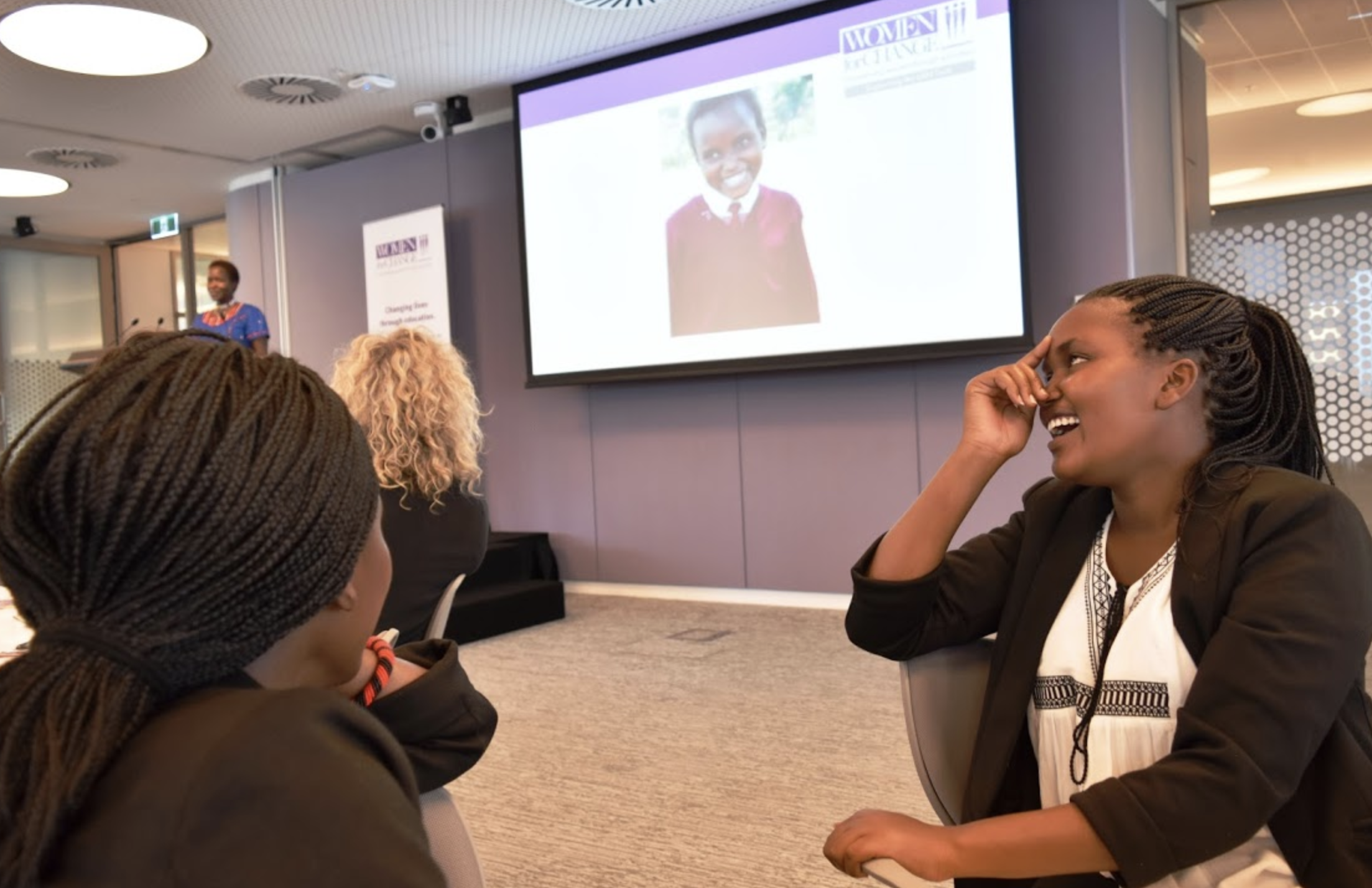 Linet laughs as Kakenya shares a photo of her as a fourth grader at KCE with the audience at the Women in Transactions luncheon.