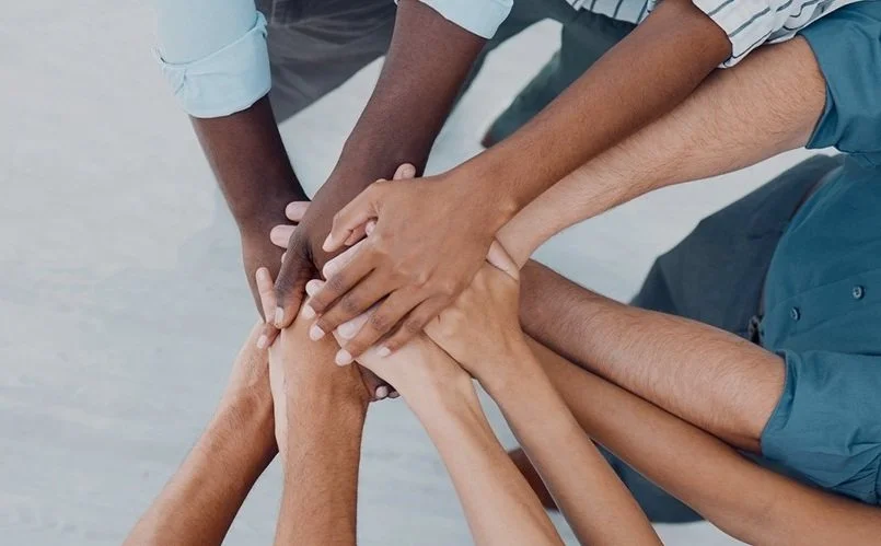 Multiple hands of diverse individuals stacked together in a display of unity and teamwork.